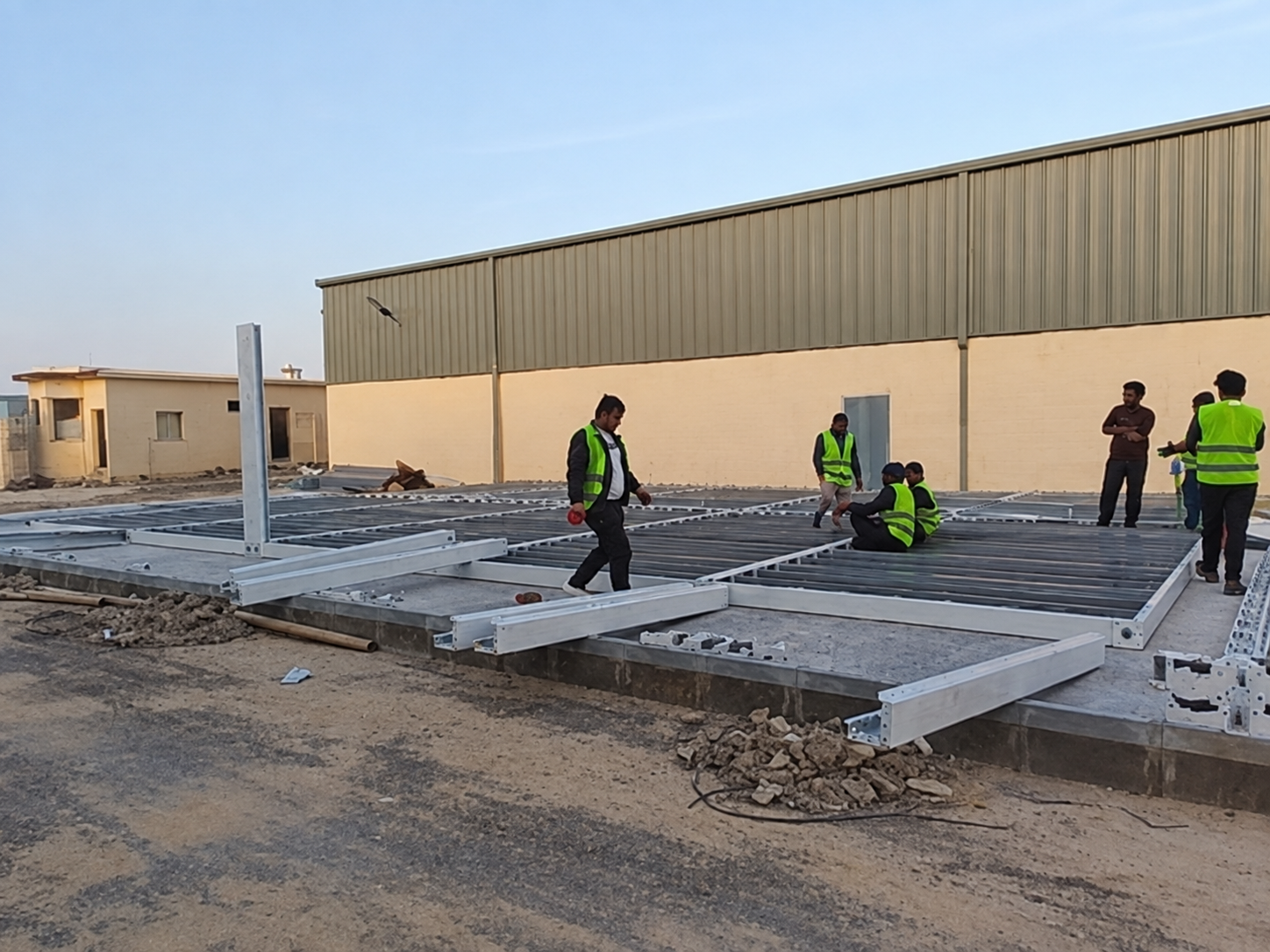 Workers assembling modular container office frames beside an industrial building in Riyadh