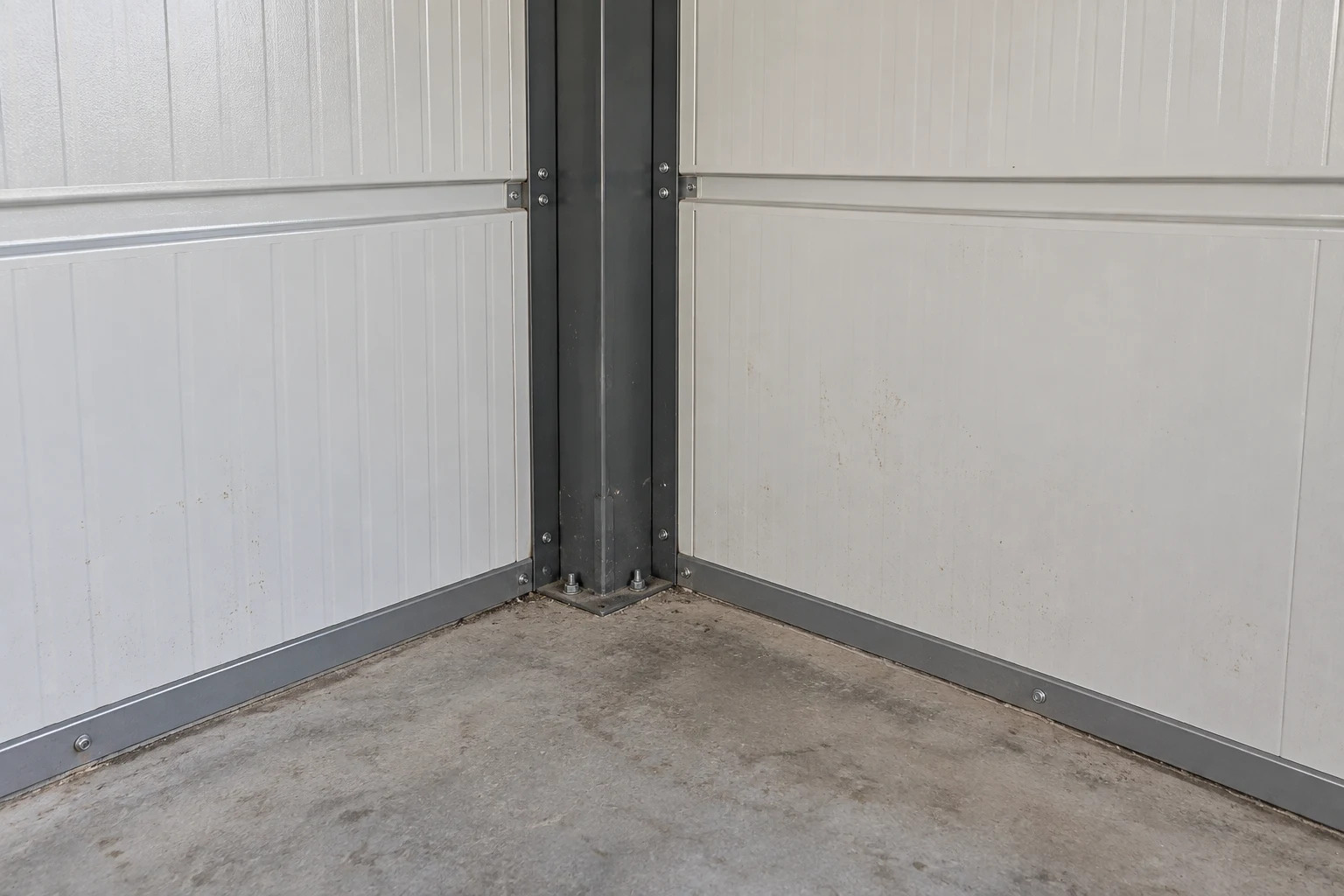 Gray steel frame, wall-panel joints and concrete floor inside a modular garage.