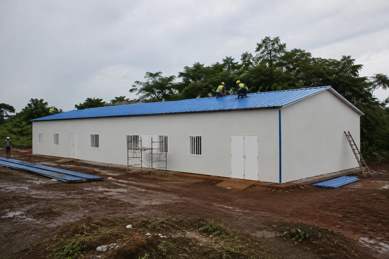 Single-storey prefab building with workers installing the blue roof