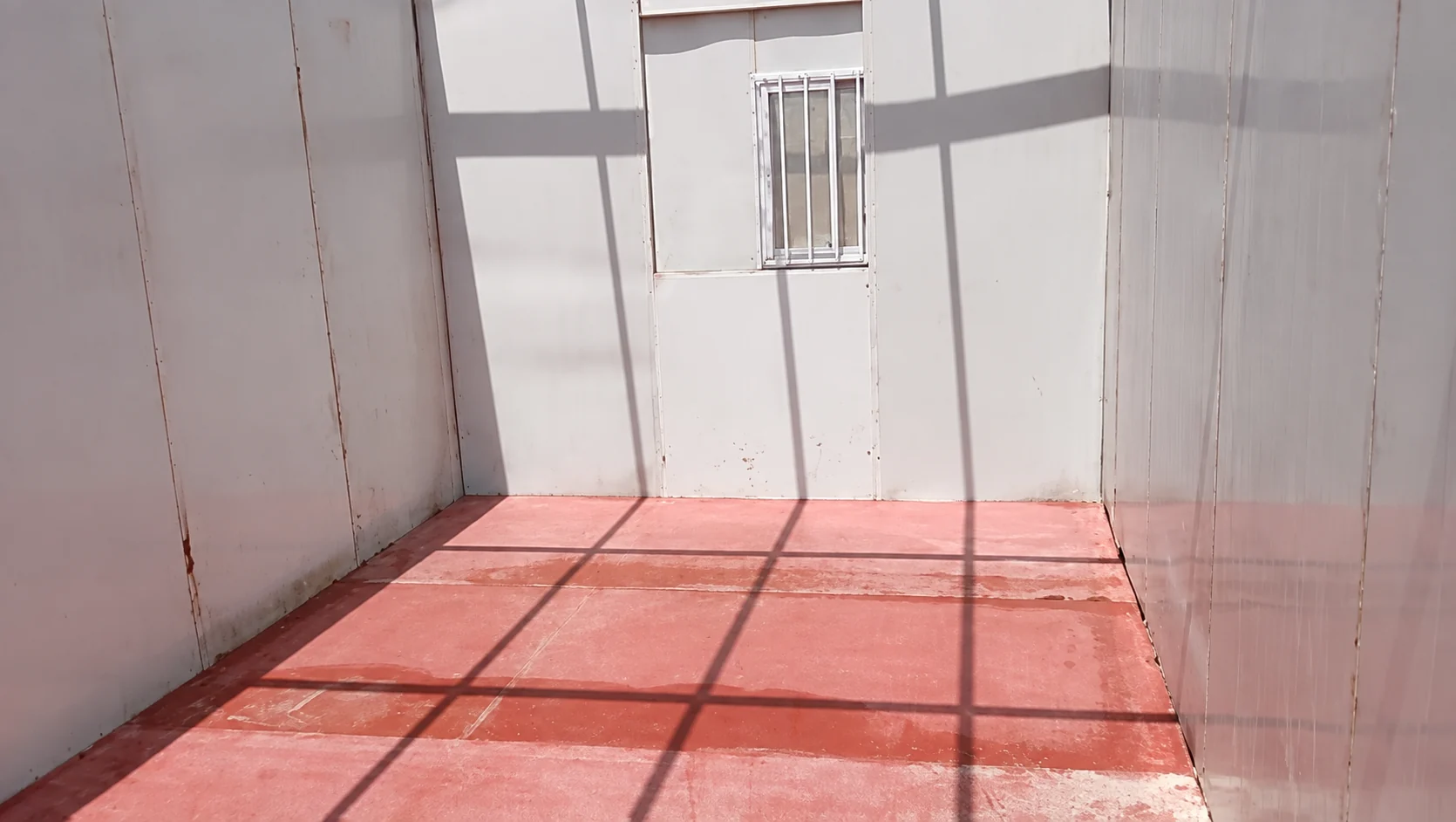 Modular room interior with white wall panels and an unfinished red floor