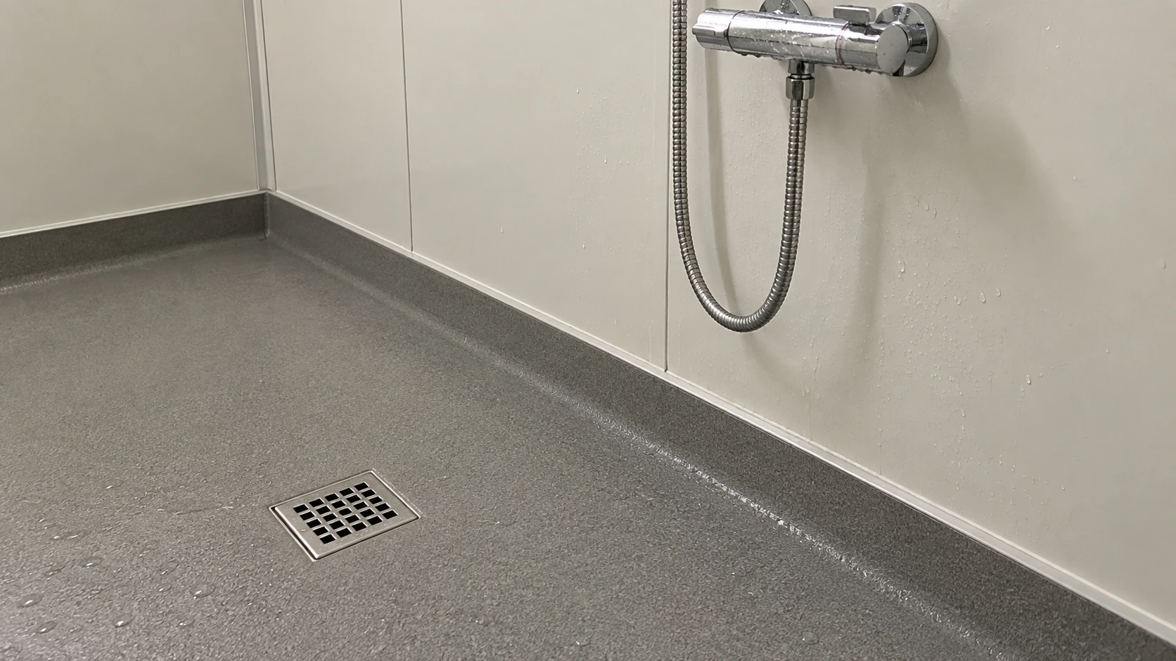 Concept detail of a shower floor drain beside a plain panel wall junction