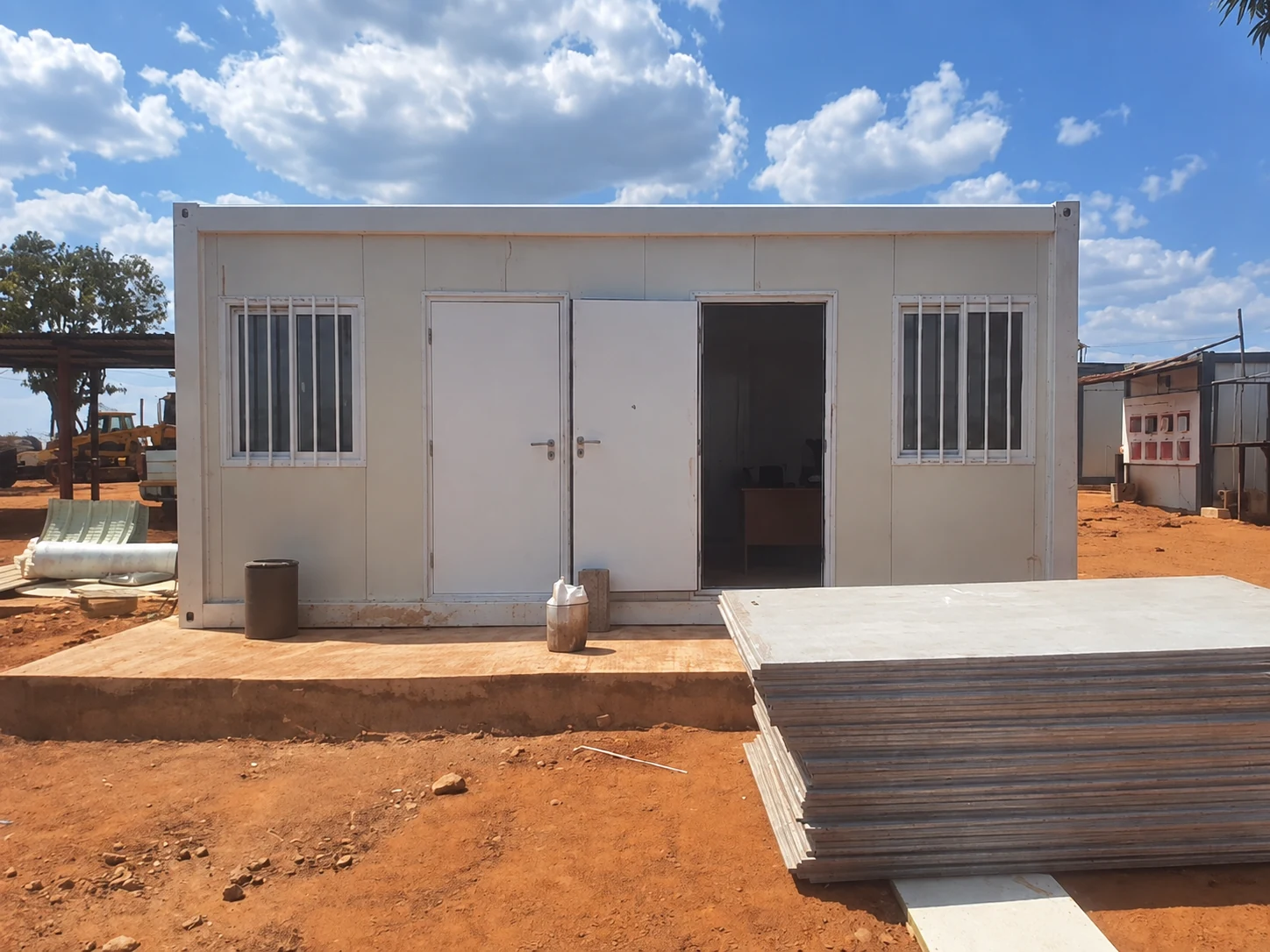 Front view of a white modular building with stacked panels in the foreground