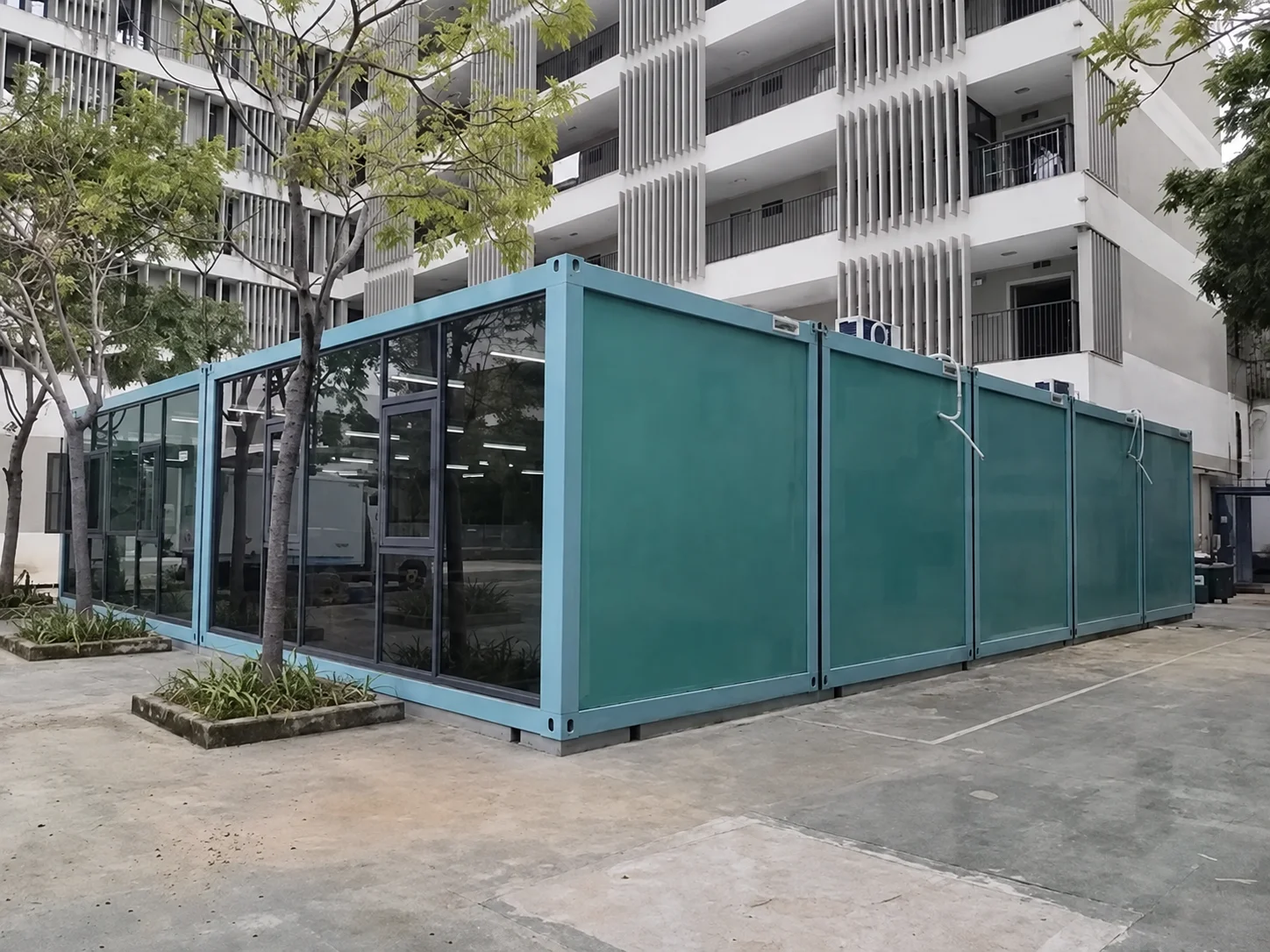 Reference turquoise modular building with a glazed front beside an apartment block