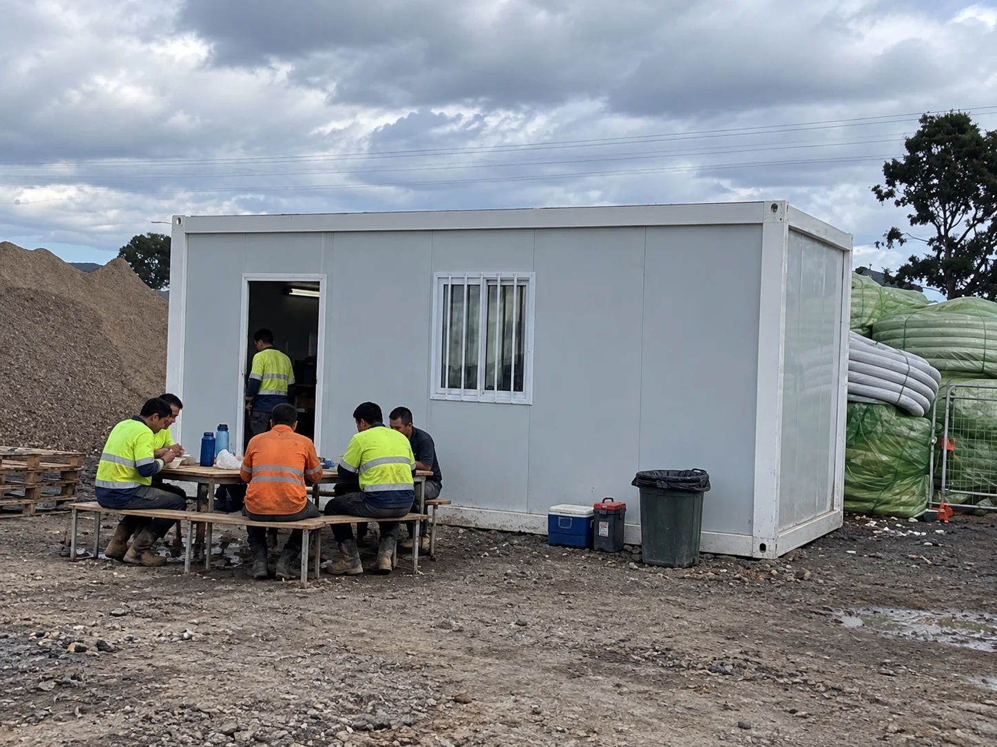 Reference people seated outside a white modular room on rough ground