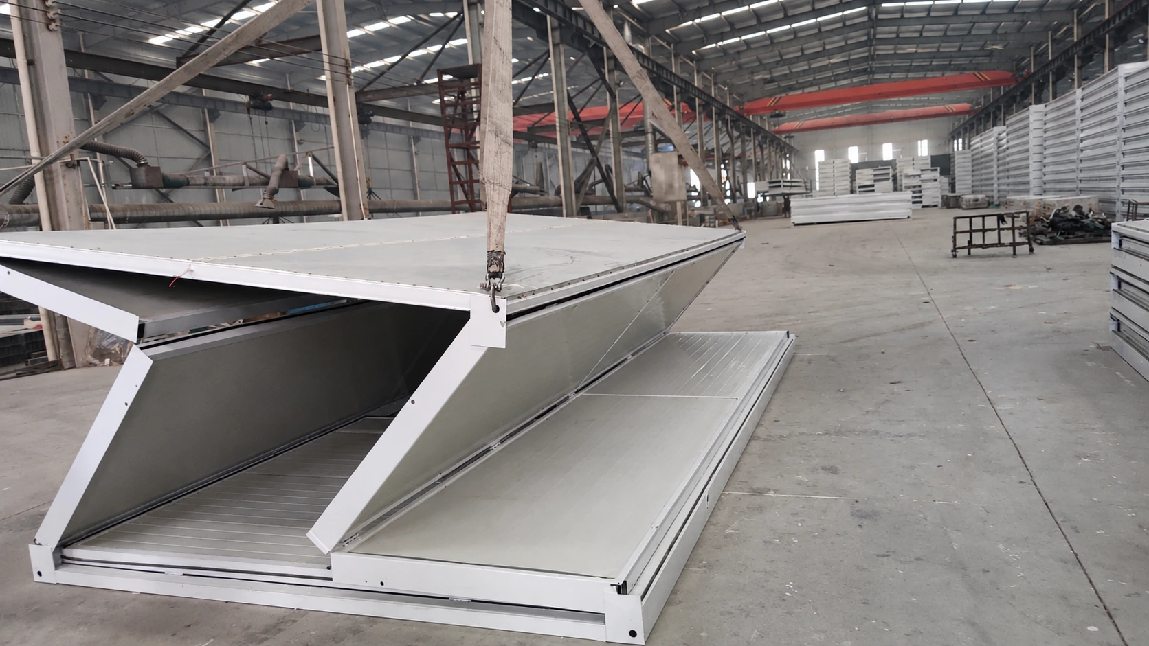 Referencia del taller de producción que muestra un techo de habitación plegable suspendido sobre paneles de pared inclinados.