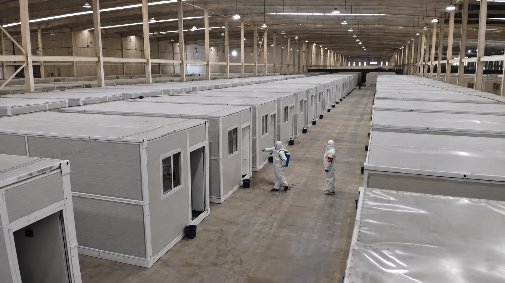 Foto de referencia de salas modulares grises dentro de un pabellón, con dos trabajadores con monos de protección junto a las puertas.