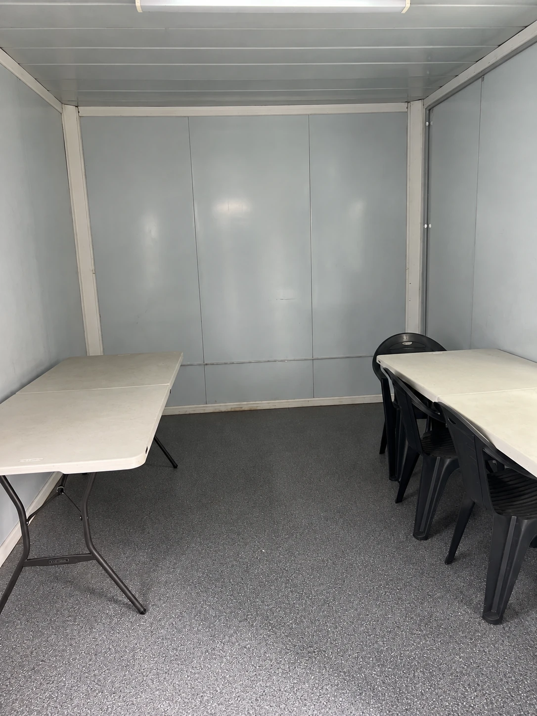 Klapptische an beiden Raumseiten, schwarze Stühle rechts und freier Mittelgang unter einer Lichtleiste. Referenz für Speiseraumnutzung.