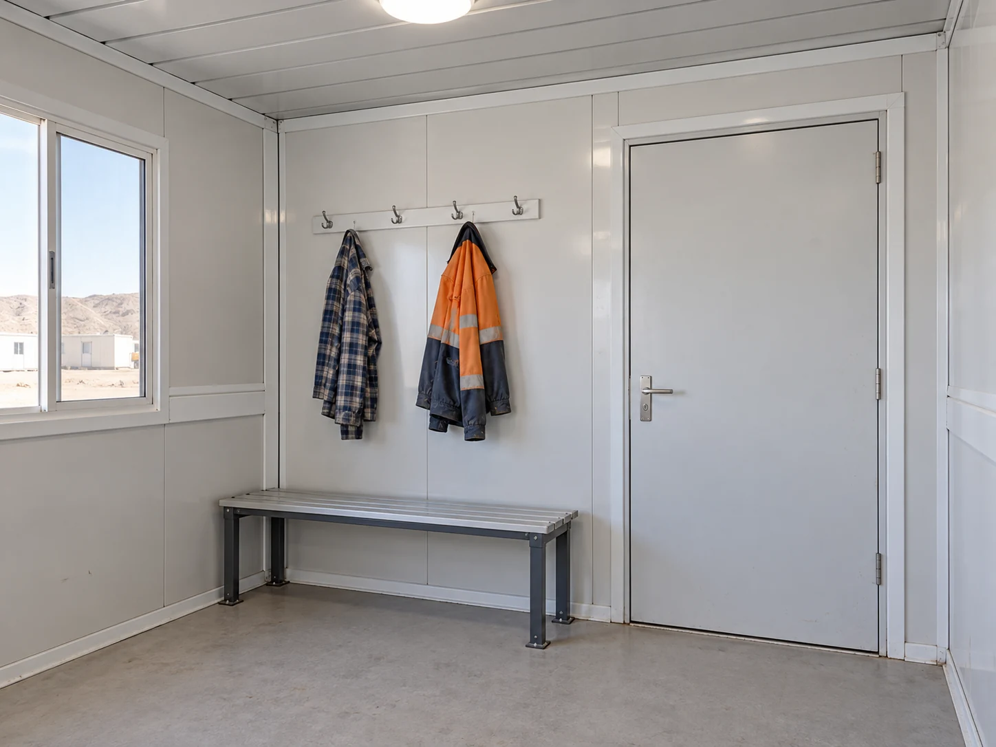 A simple enclosed changing place with a bench and clothing hooks beside a closed door