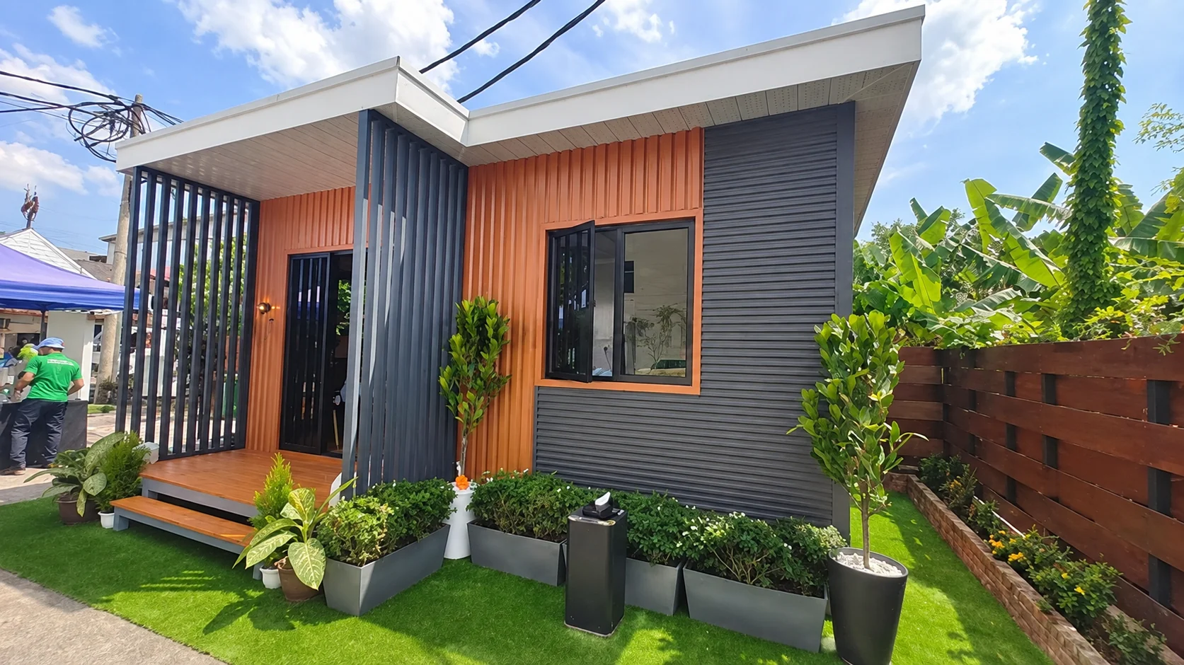 Vista em ângulo do edifício modular do projeto na Tailândia, com uma divisória de entrada e degraus frontais ajardinados.