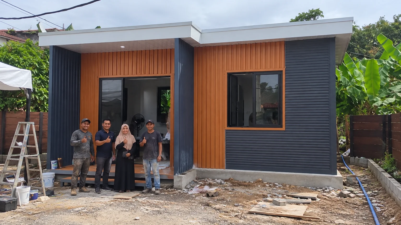 Pessoas em pé do lado de fora de um edifício modular laranja e cinza escuro no projeto da Tailândia.