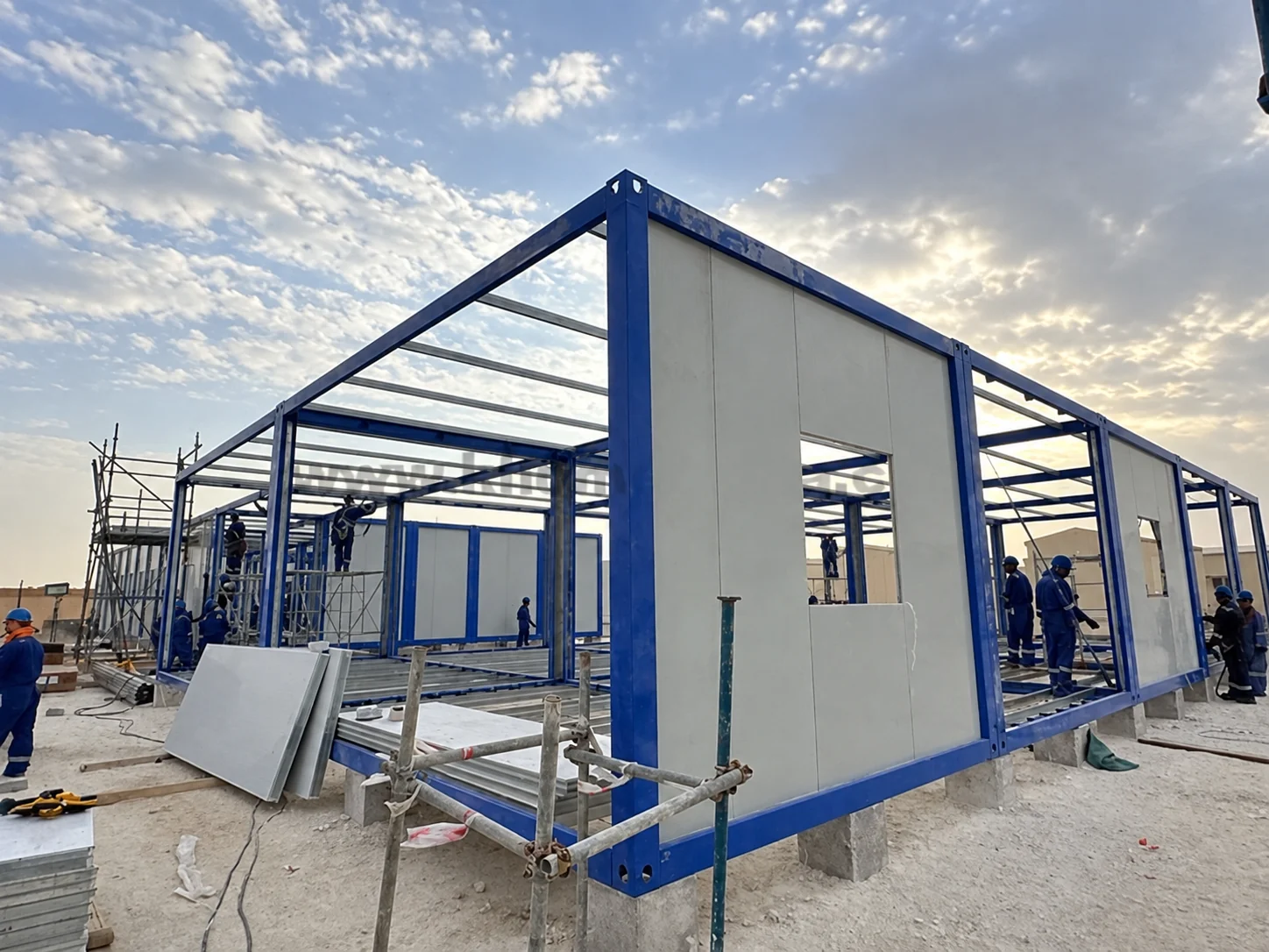 Trabajadores colocando paneles blancos en una estructura modular azul en la obra de Omán.