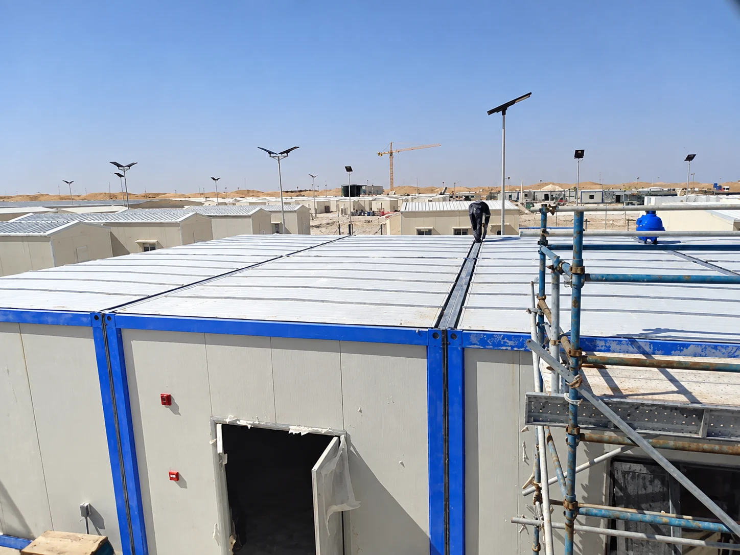 Trabajadores en los techos de las unidades modulares blancas y azules en la obra de Omán.