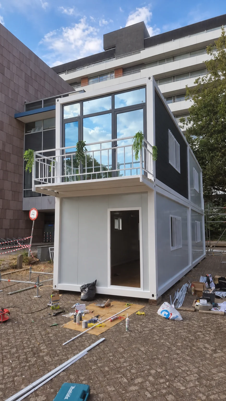 Portfólio de referência mostrando um edifício modular estreito de dois andares com fachada superior envidraçada.