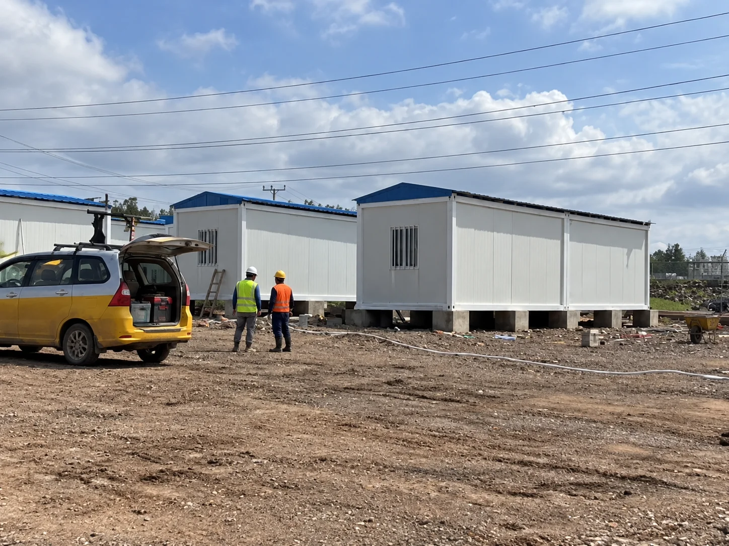 Referenzbild eines modularen Gebäudes mit erhöhten weißen Hütten und Arbeitern auf einer unfertigen Baustelle.