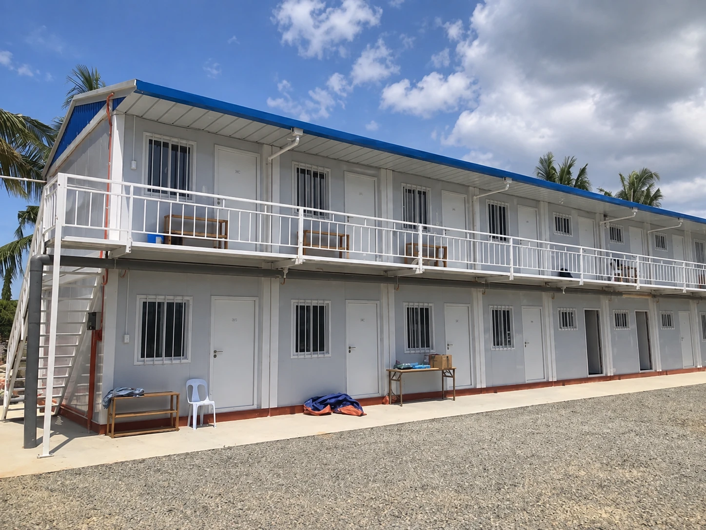 Two-storey modular block with an upper balcony, white railing, blue roof edge and barred ground-floor windows. Shared exterior reference.