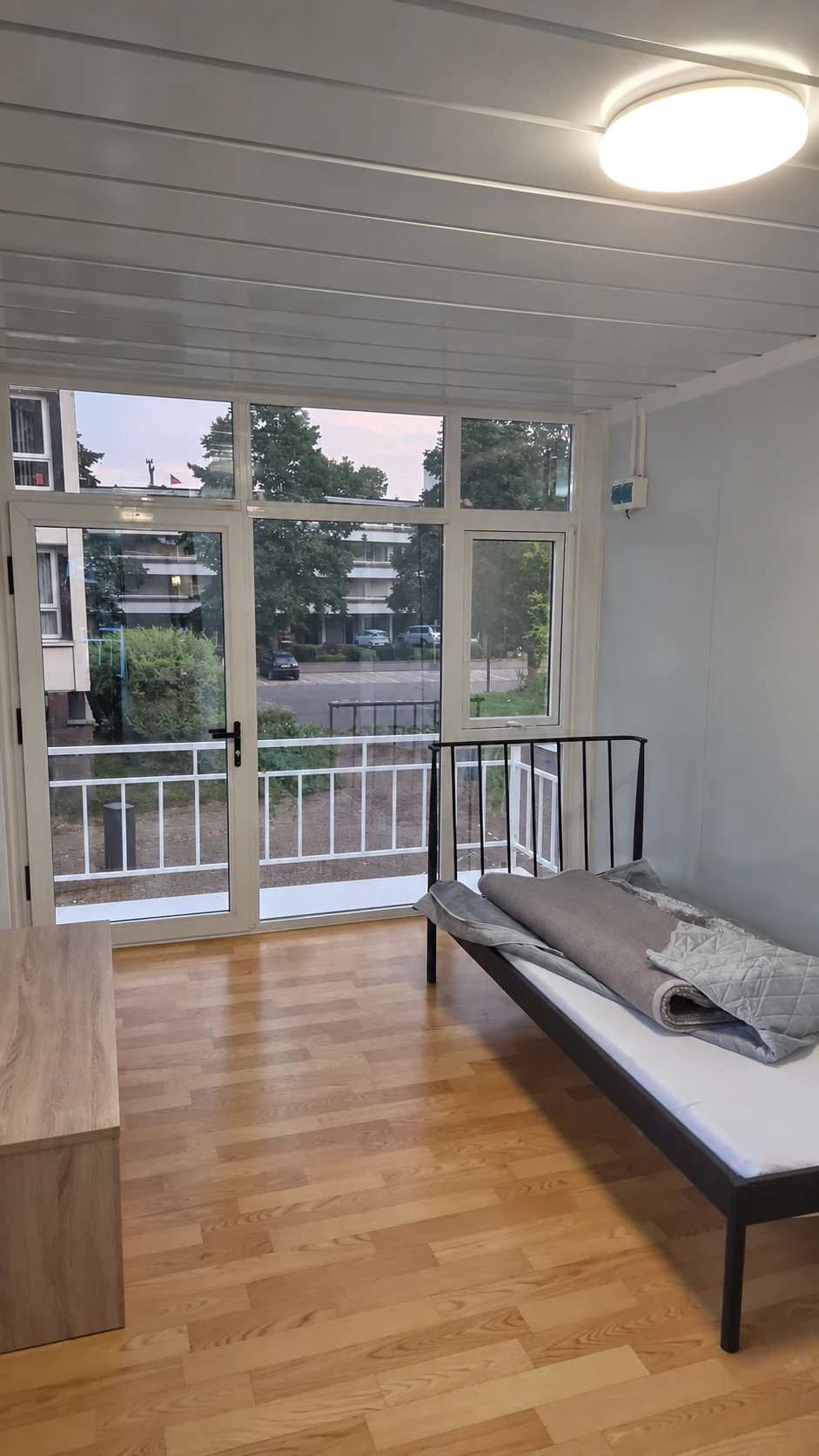 Single bed beside full-height glazing and a glazed balcony door in a compact wood-floored room. Bedroom layout reference.