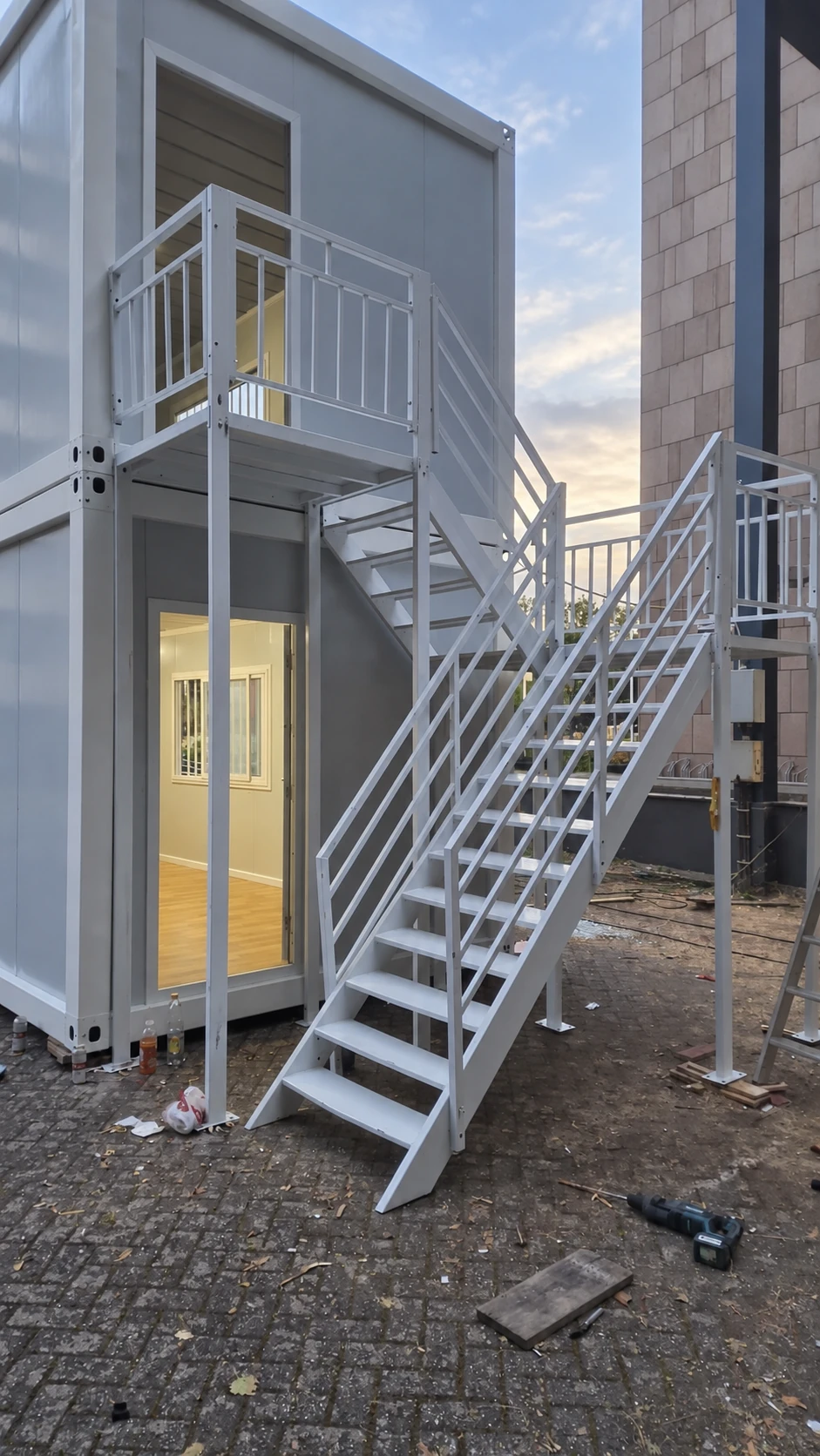 White external steel staircase and guarded landing connecting the upper doorway of a two-storey module. Circulation reference.