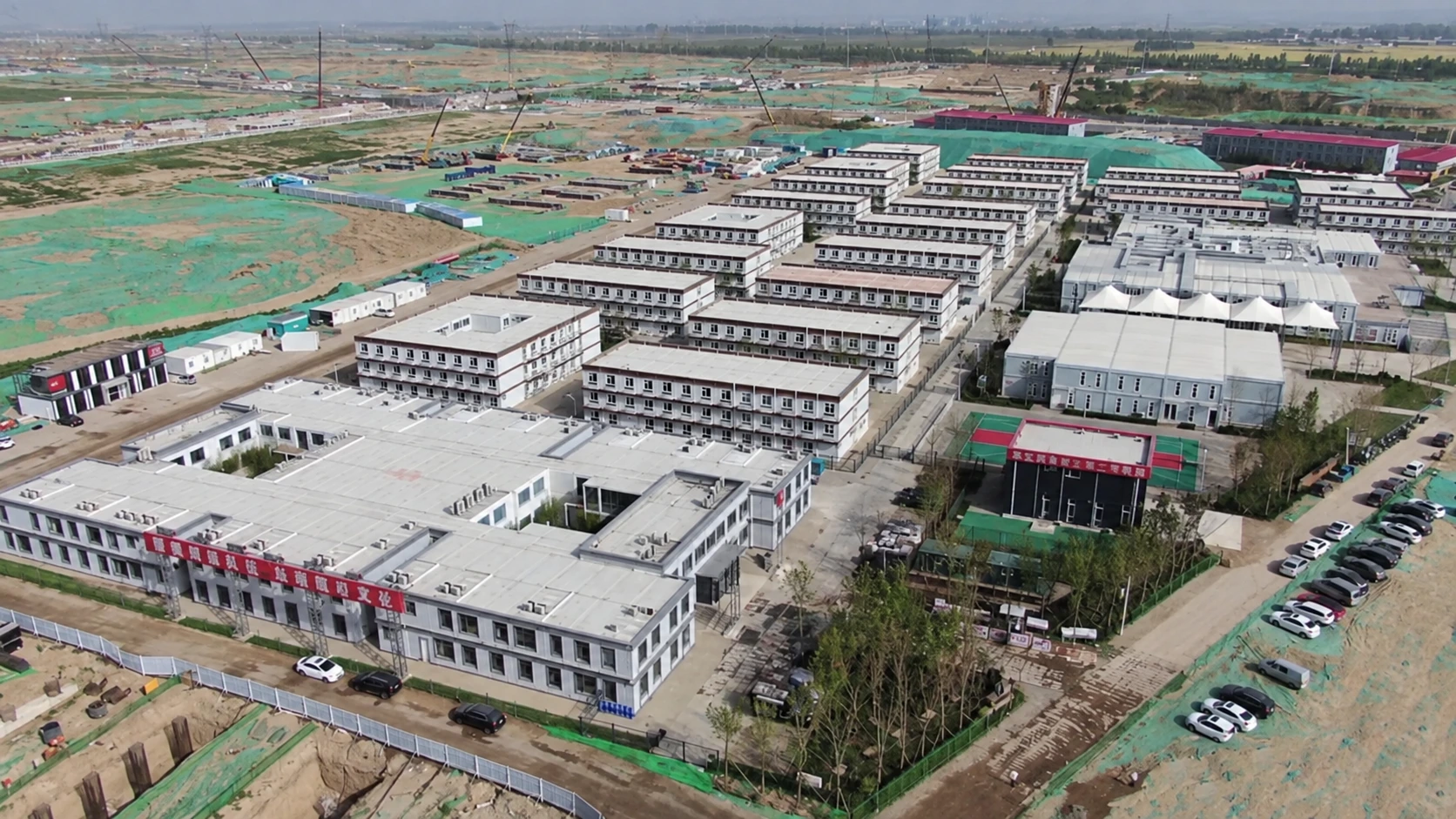 Fotografía aérea de referencia de un gran complejo de edificios modulares con largos bloques paralelos y zonas de construcción alrededor de su perímetro.