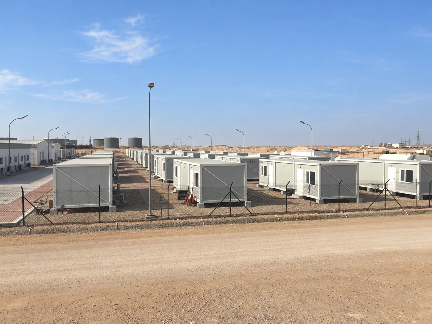Fotografía exterior de referencia que muestra hileras valladas de habitaciones modulares de una sola planta a lo largo de un camino de acceso recto.