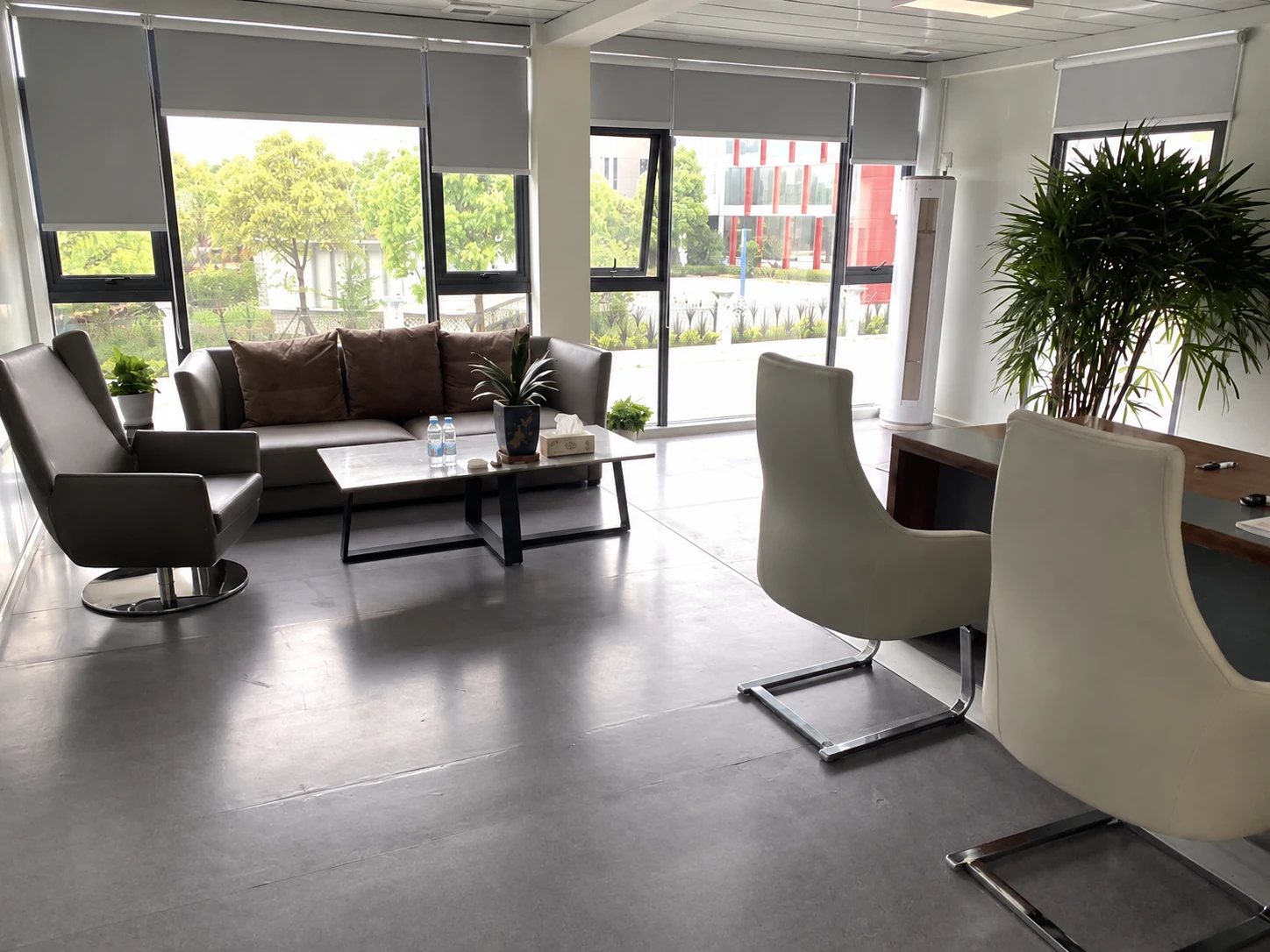 Lounge chairs, sofas, plants and broad windows in a modular room; wider room-use reference.