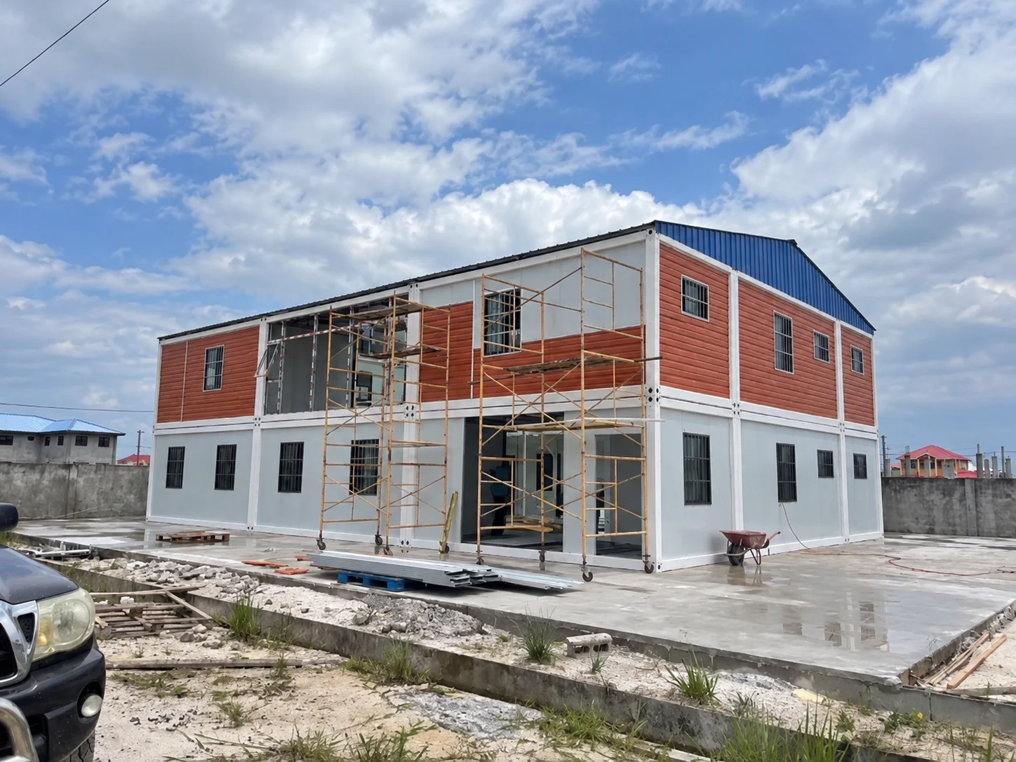 Photographie de référence d'un bloc modulaire blanc et orange avec un toit en pente et des échafaudages.