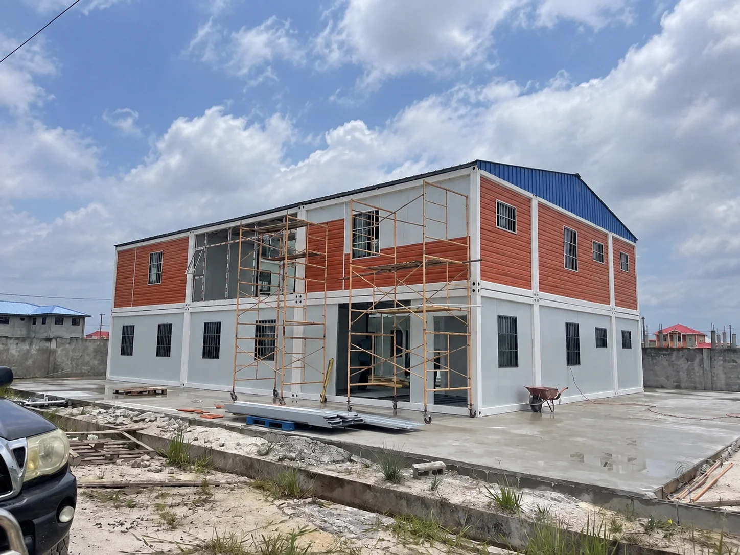 Portfólio de referência mostrando um edifício modular de dois andares em vermelho e branco com andaimes.