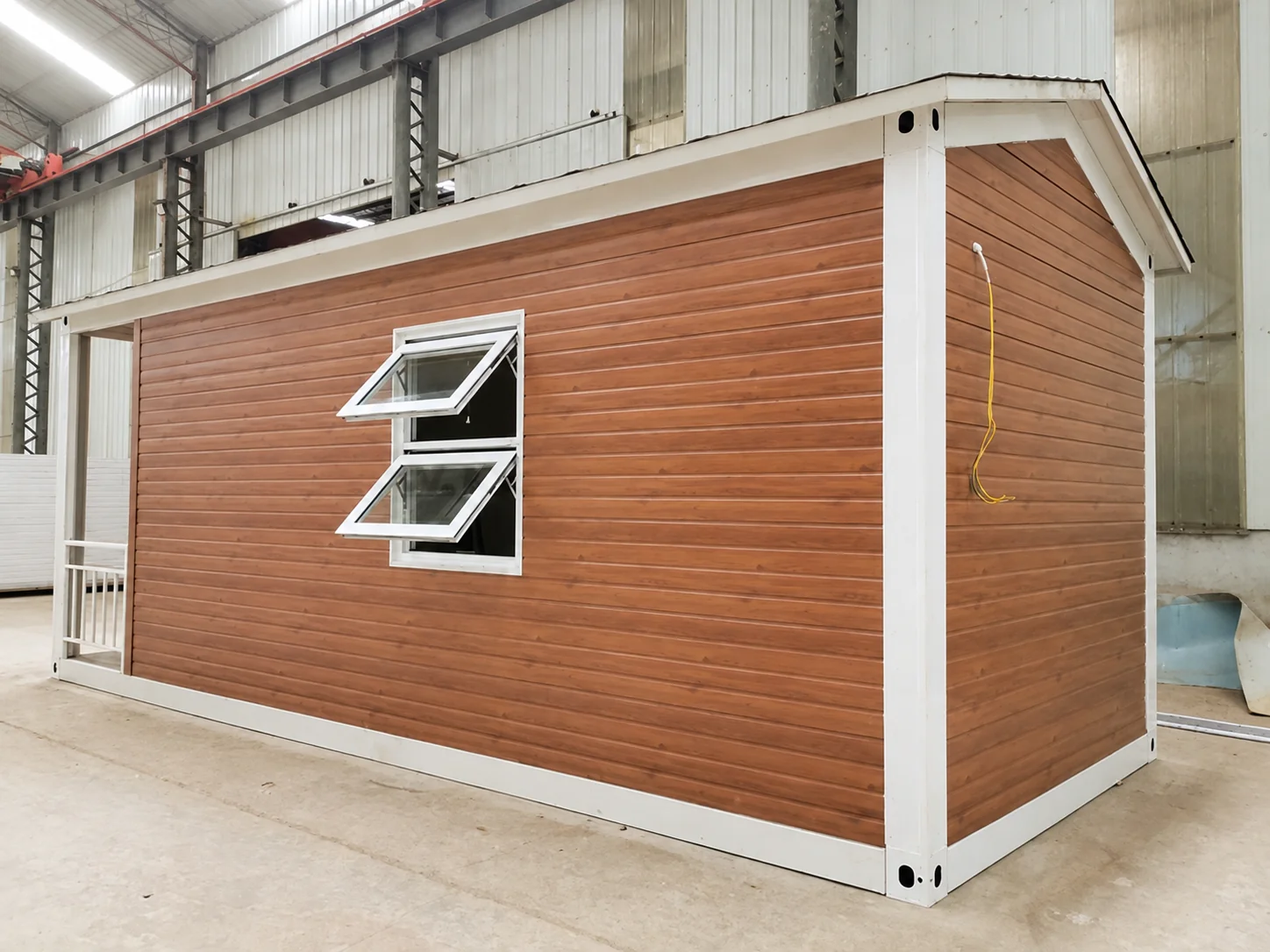 Imagem de referência de oficina mostrando uma cabana modular revestida com acabamento em madeira e com janela basculante aberta.