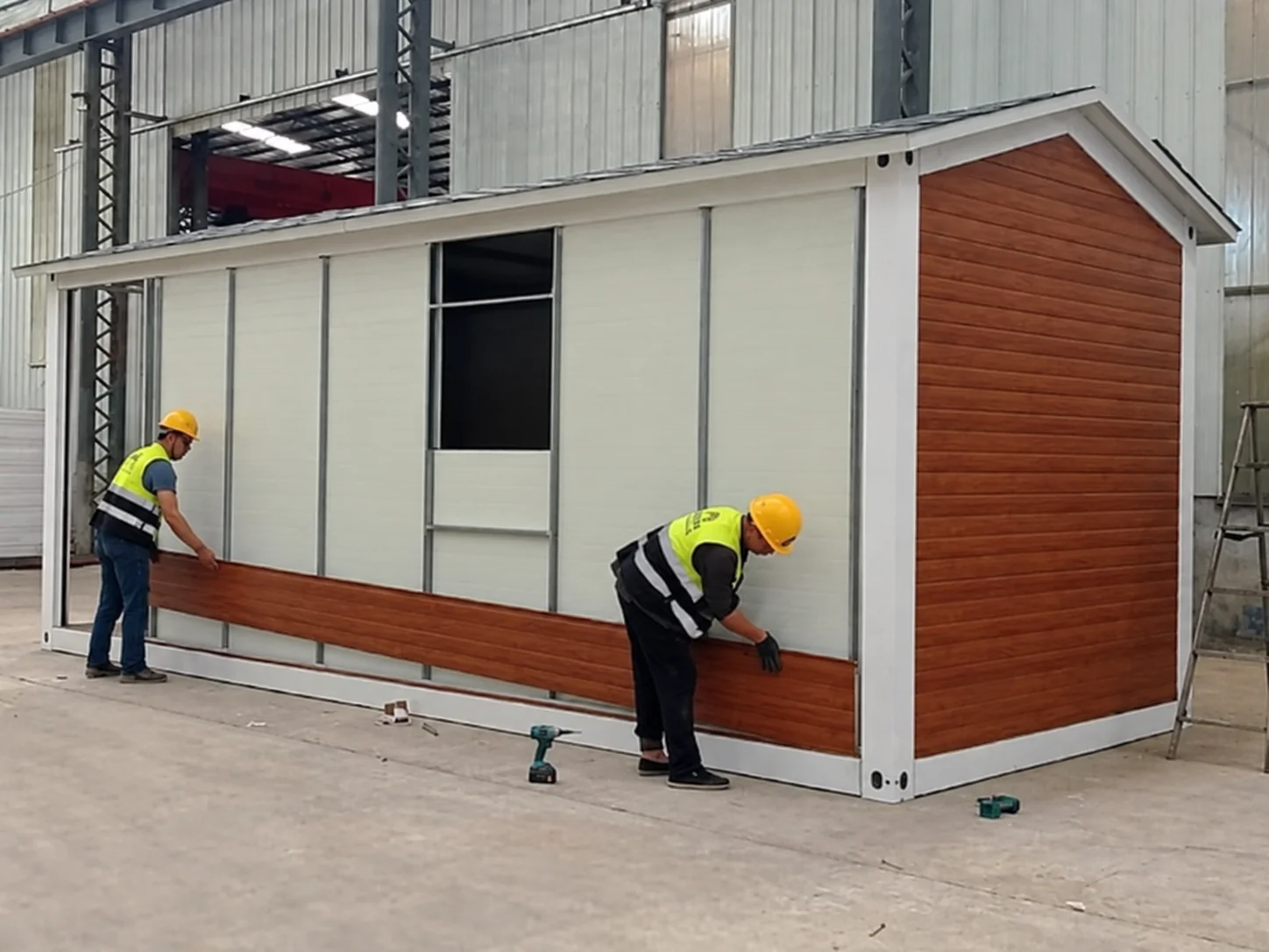 Referência de oficina mostrando trabalhadores instalando revestimento horizontal em uma cabine modular.