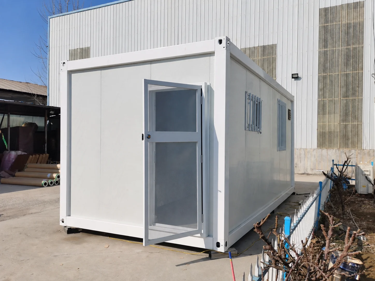 Vues latérale et frontale d'un module de pièce blanche avec une porte d'entrée vitrée ouverte dans une cour d'usine. Référence de fabrication.