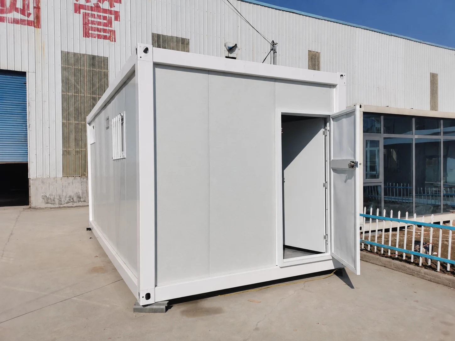 Module blanc de chambre avec porte battante ouverte dans une cour d’usine. Référence de fabrication.