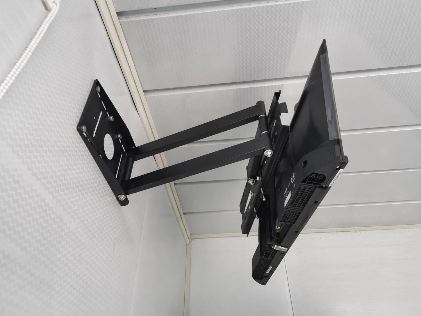 Vue latérale d'un support de télévision articulé et étendu, fixé au mur d'une salle d'échantillons. Référence du composant.