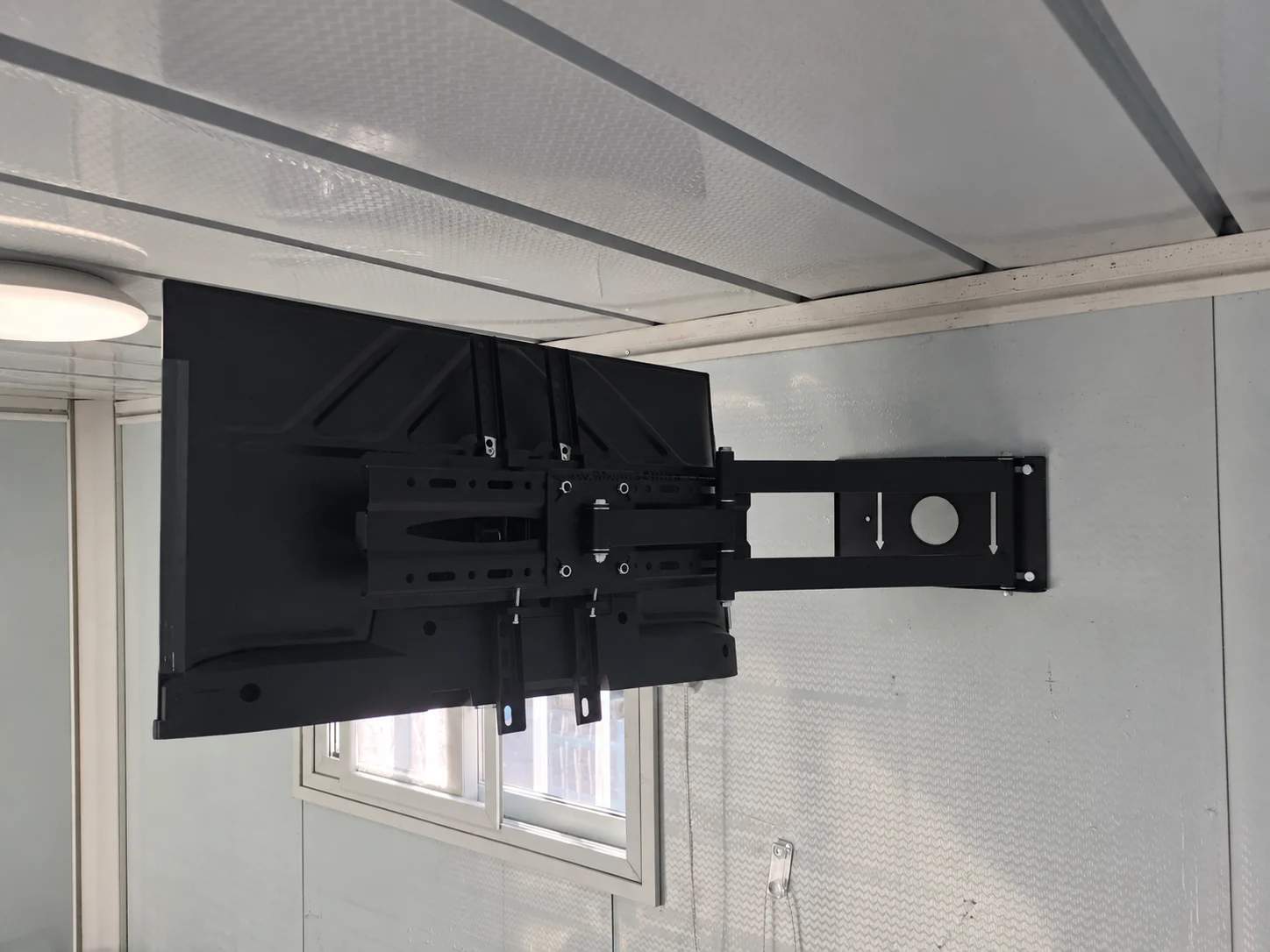Vue arrière d'un téléviseur et de son support mural pliable dans une pièce modulaire type. Référence des composants.