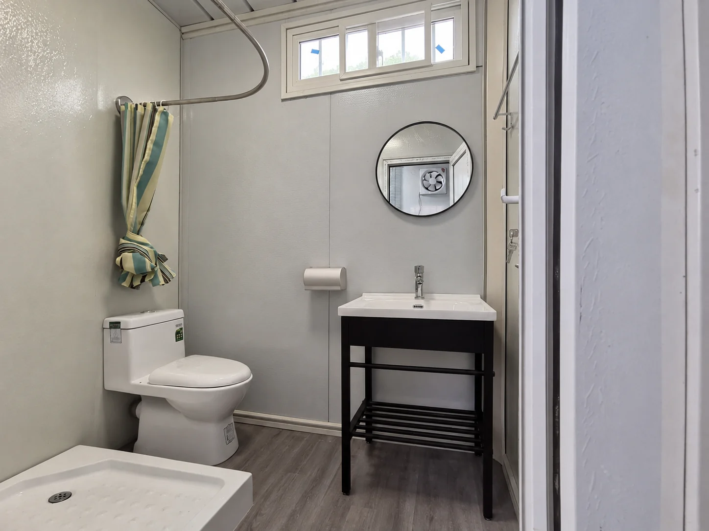 Exemple de salle d'eau avec WC, rideau de douche, lavabo et miroir rond. Référence d'aménagement intérieur.