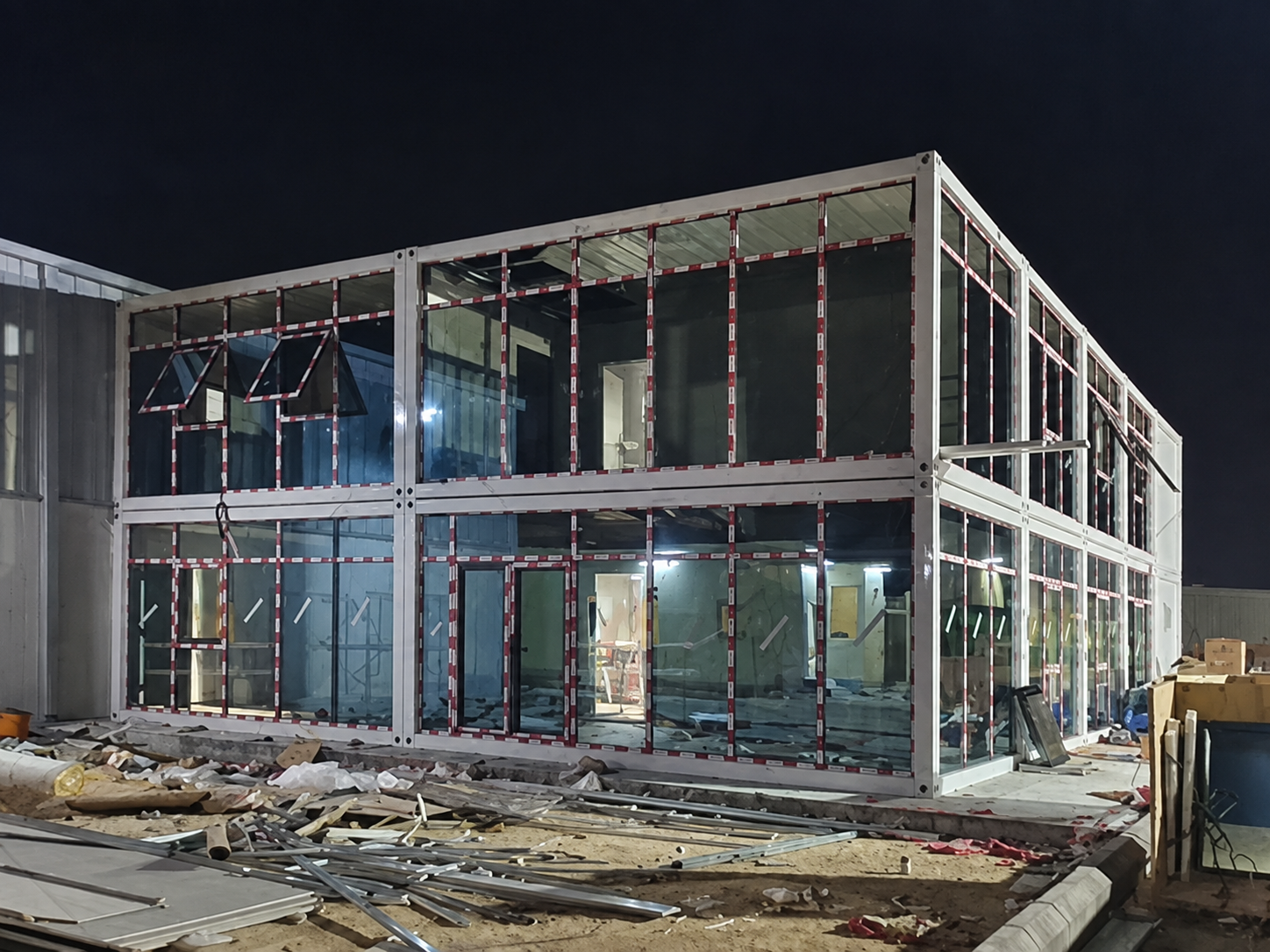 Fachada envidraçada de um edifício de escritórios de dois andares construído em contêineres, fotografada à noite em Riade.