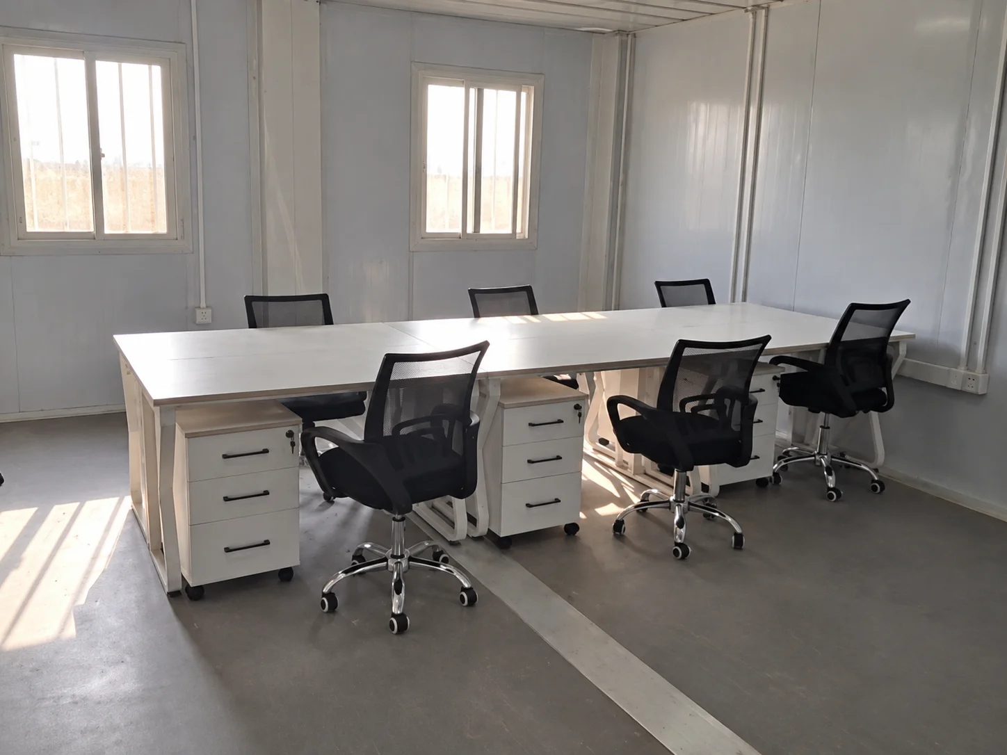 Referenzbüro-Interieur mit Schreibtischen und Drehstühlen neben großen Fenstern.