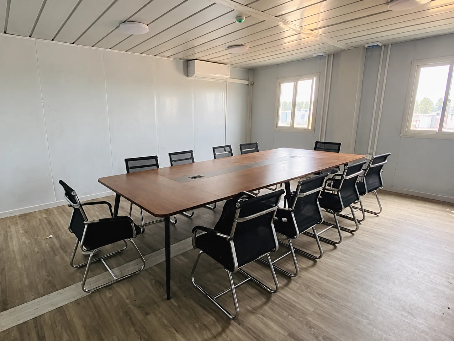 Referenz-Besprechungsraum mit einem langen Holztisch, schwarzen Stühlen und Fenstern.