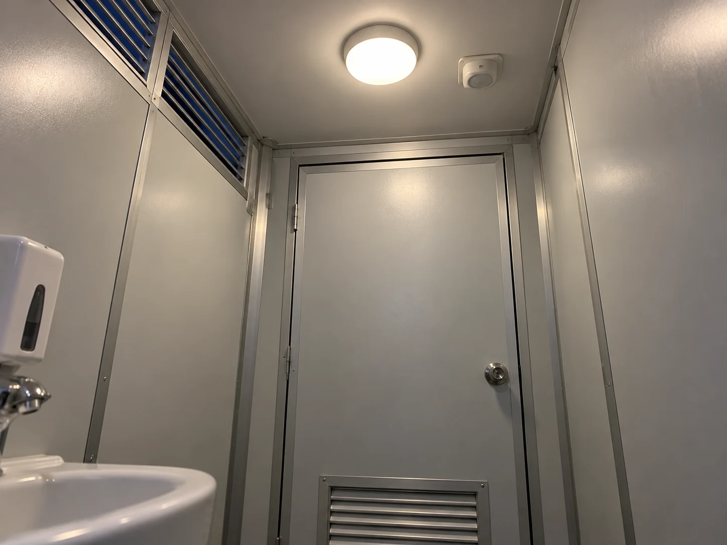 A simple ceiling light and small control unit above a sanitation-cabin doorway