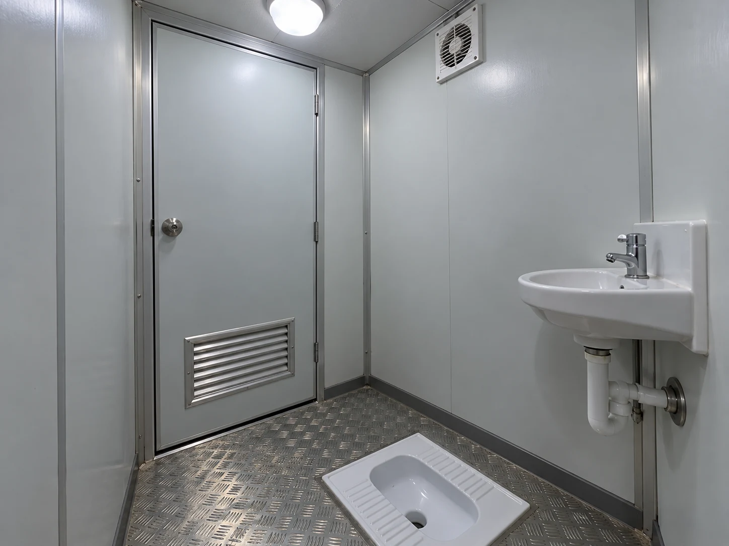 A simple private toilet cabin with a squat toilet and small washbasin under interior light