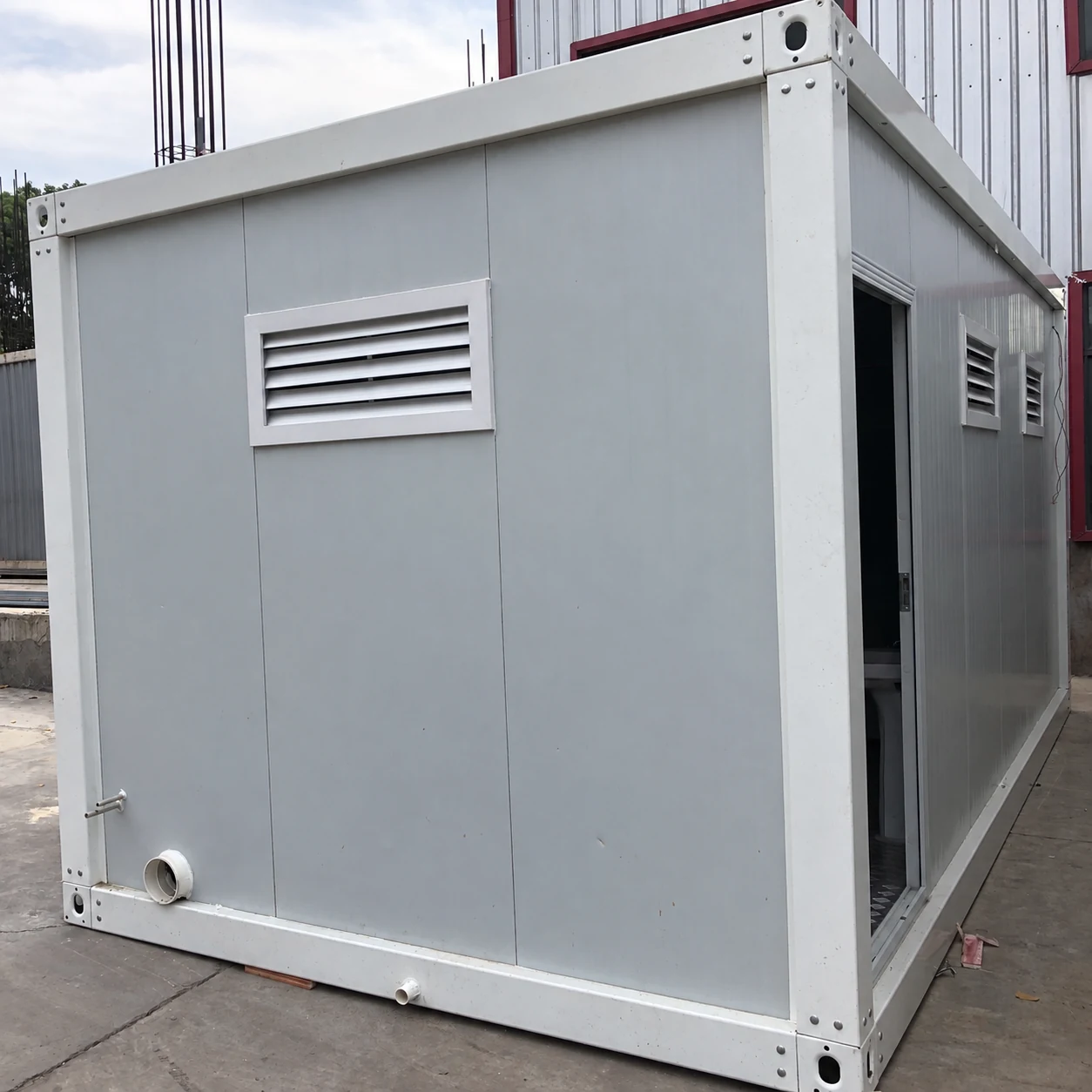 Rear face of a white portable wet-room module with a louvred vent and low outlet; product reference.