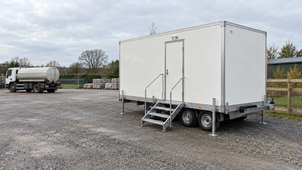 Generated illustration of a modest portable washroom trailer with clear entrance space and a service vehicle parked separately.