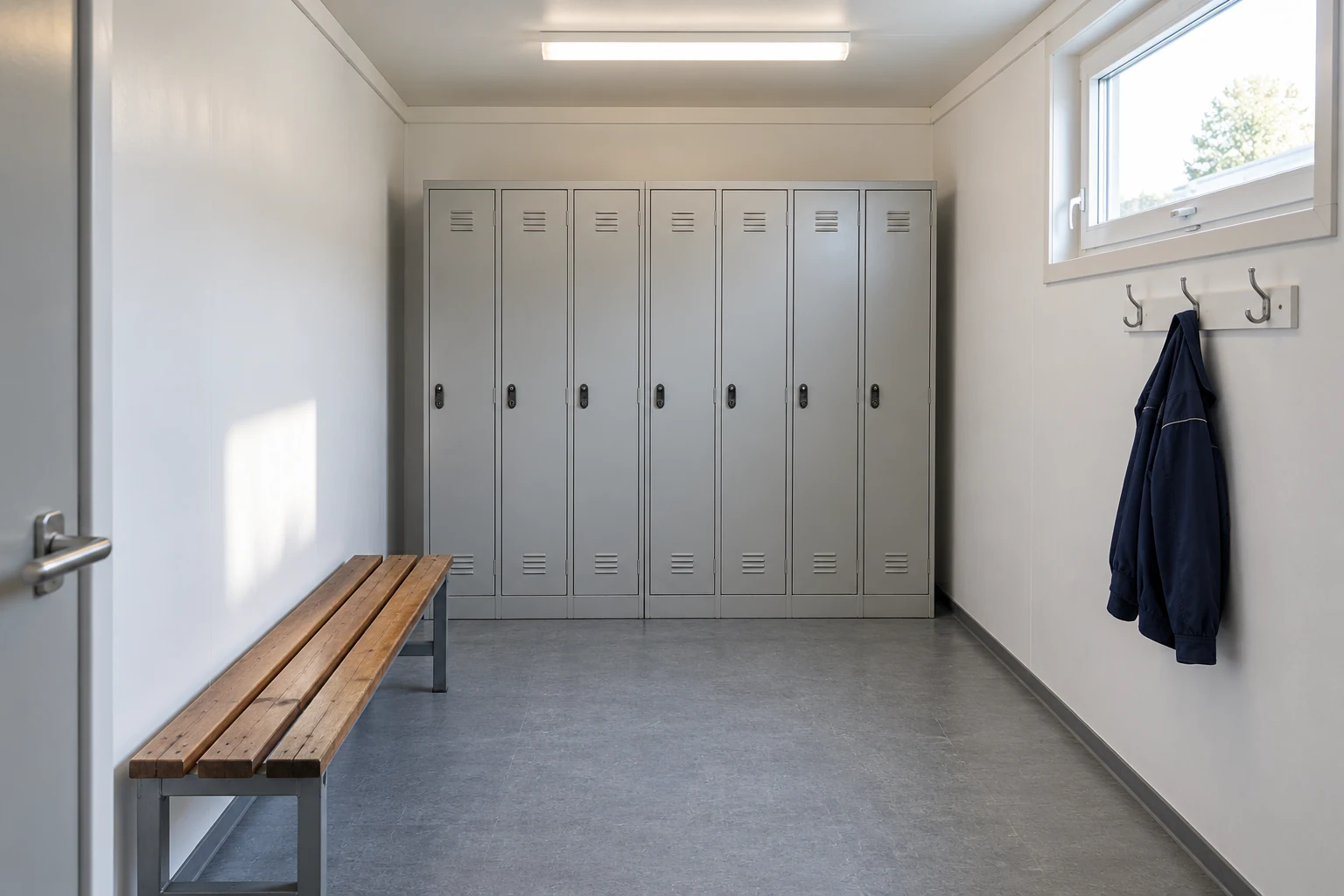A modest changing room has a bench, lockers and coat hooks.