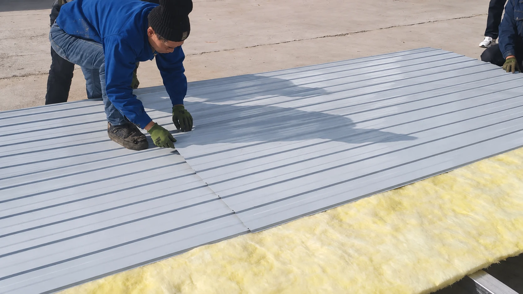 Ouvrier accroupi sur une tôle ondulée lors de l'assemblage d'un châssis de plancher dans une aire de production. Référence de fabrication.