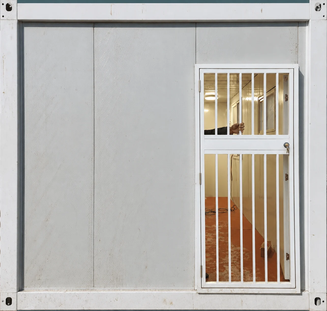 Vue de face d'une paroi modulaire blanche équipée d'une porte vitrée et de barreaux de sécurité verticaux. Référence du composant.