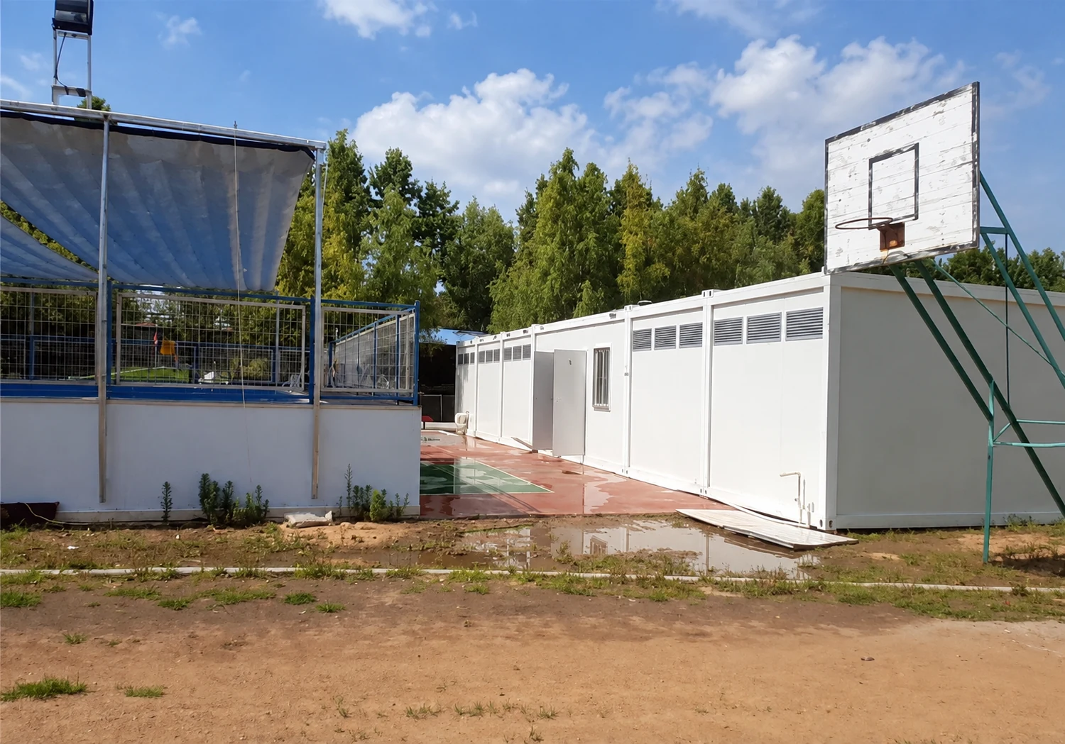 White sanitation block beside a basketball court and paved courtyard; location-unverified exterior reference.