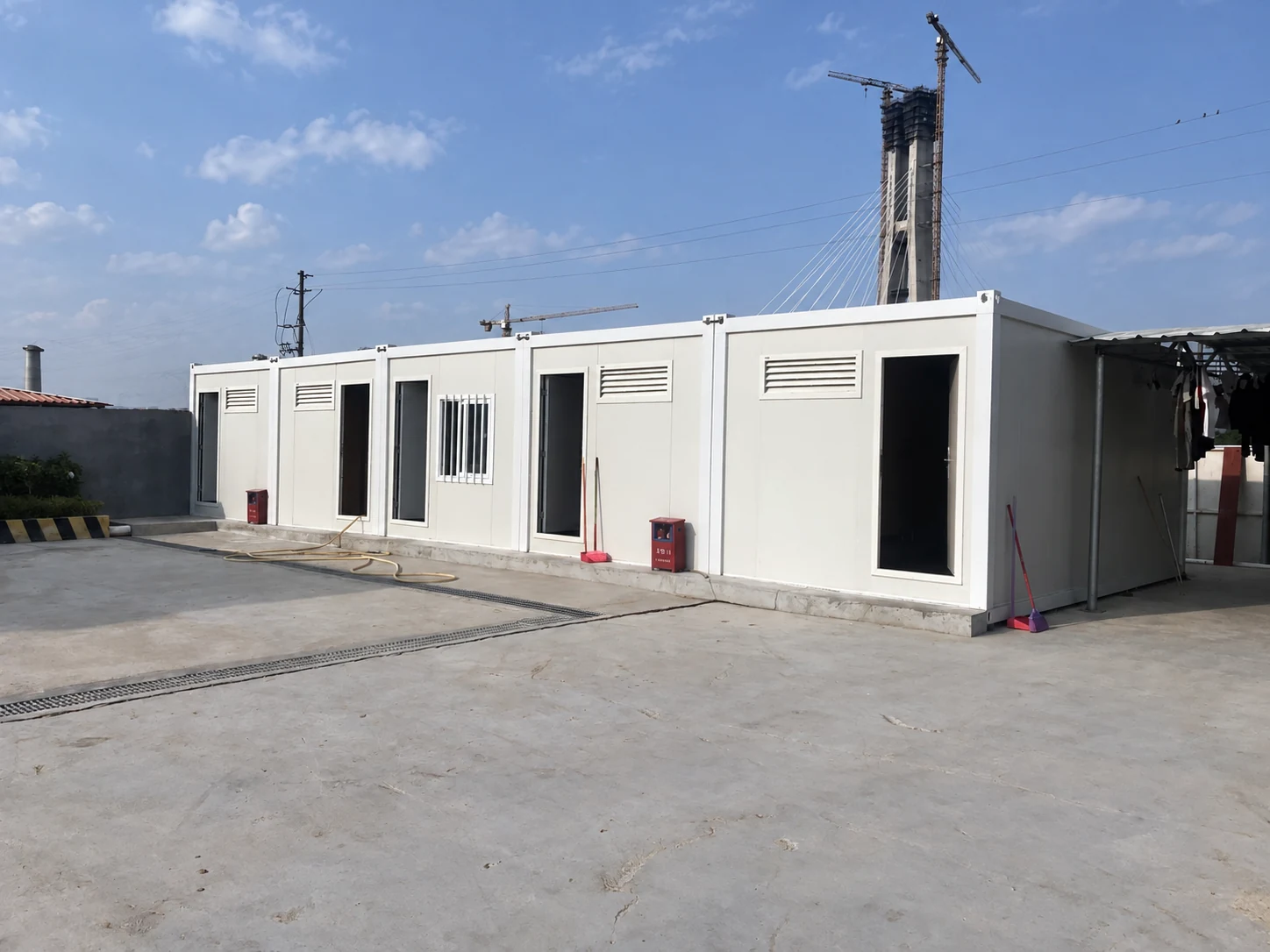White modular sanitation block with separate cubicle doors in a paved yard; exterior reference.