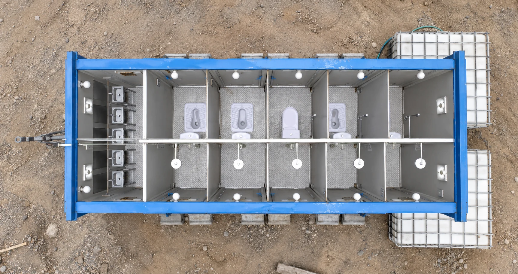 Roofless cutaway reference showing toilet cubicles and washbasins arranged within a blue-framed sanitation module.
