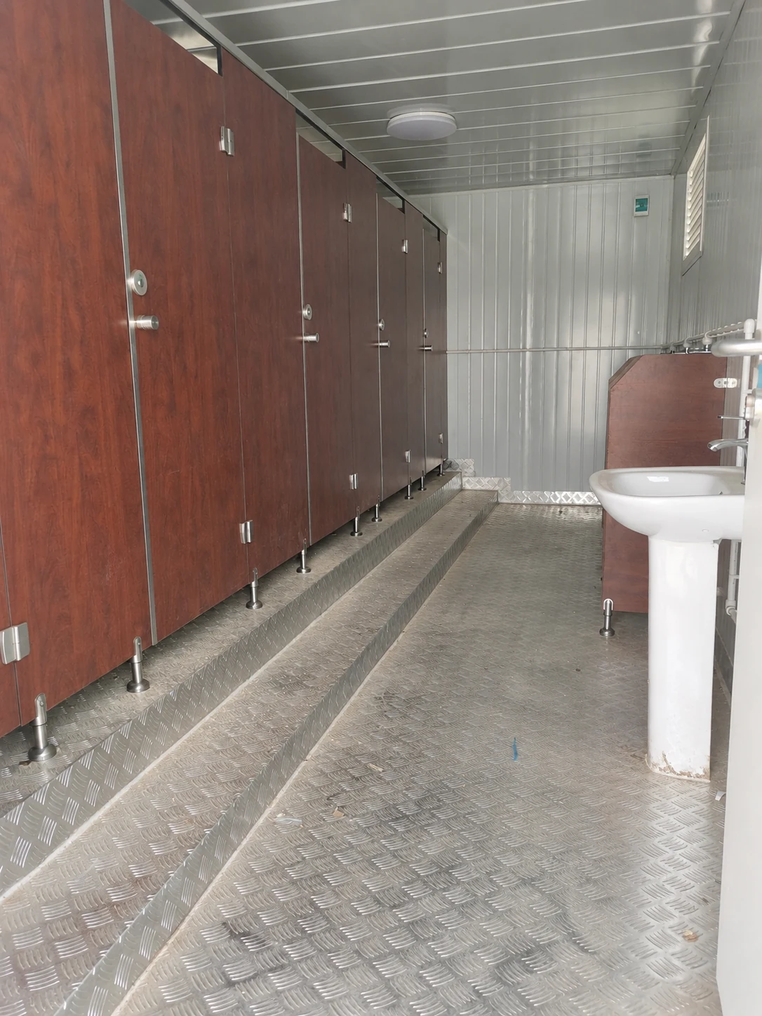 Interior reference showing brown cubicle partitions, a raised floor edge and white handwashing basins.