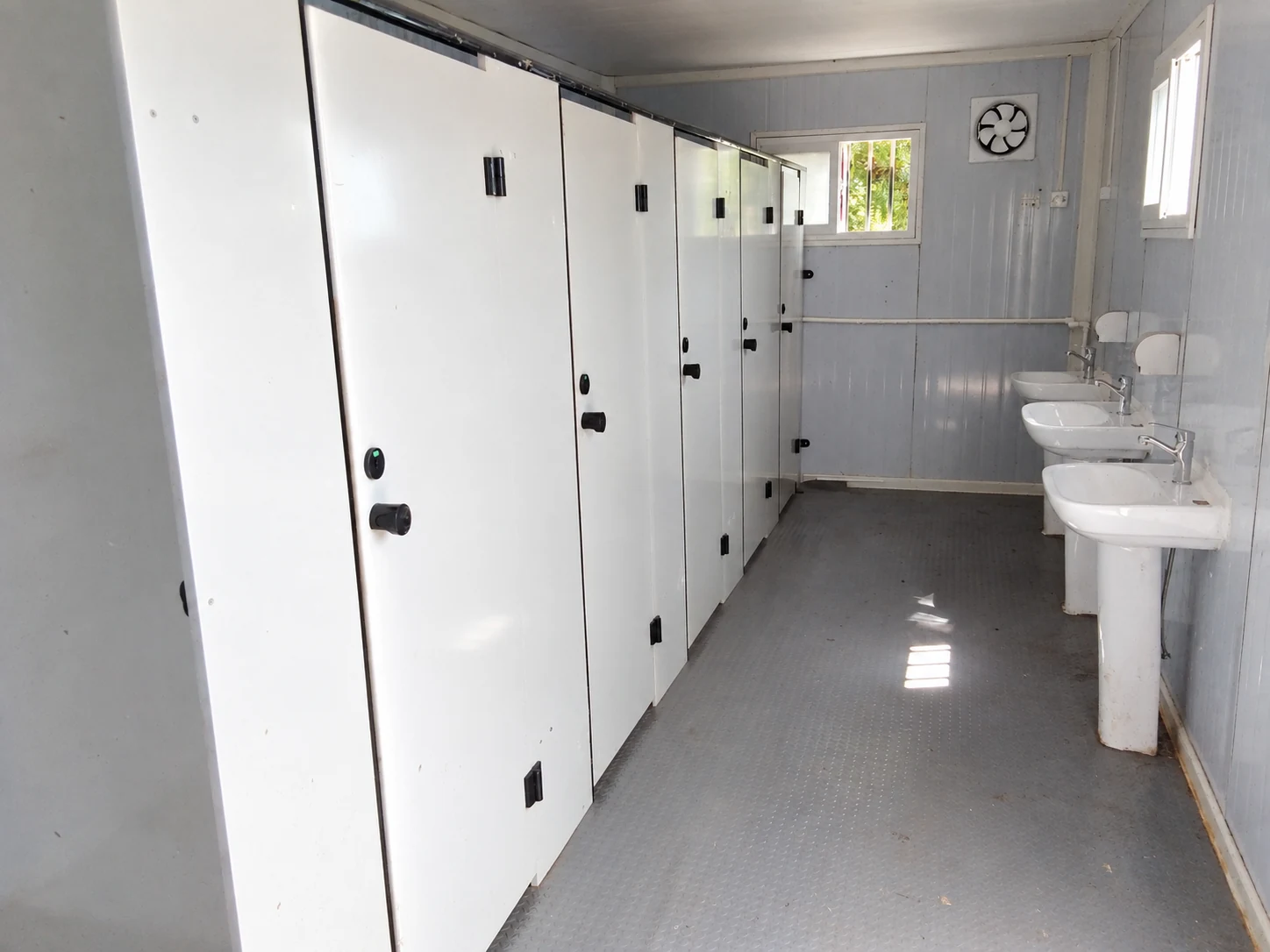 White cubicle partitions, handwashing basins and a continuous aisle floor; sanitation interior reference.