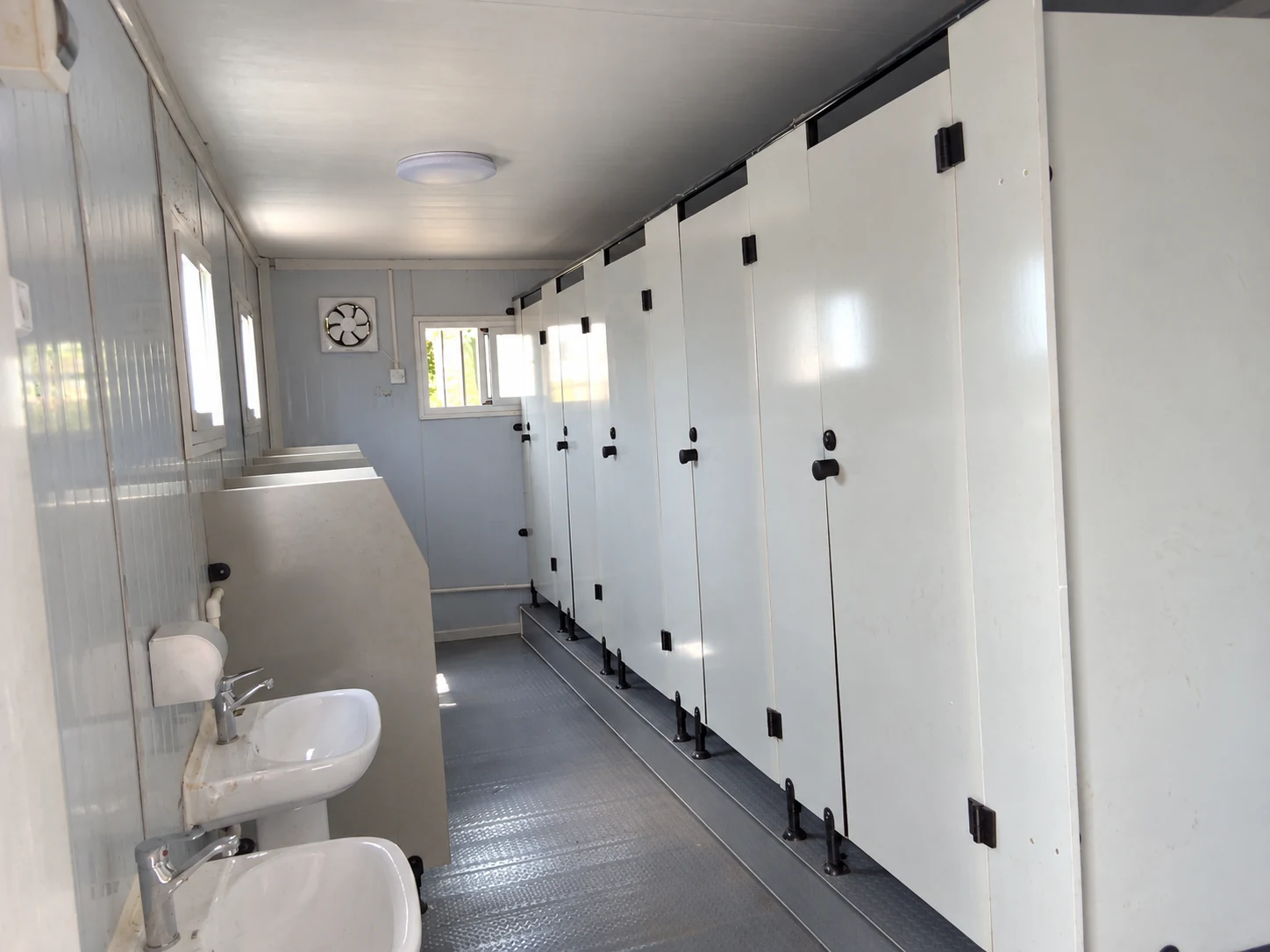 White toilet cubicles on a raised floor beside a row of handwashing basins; sanitation interior reference.